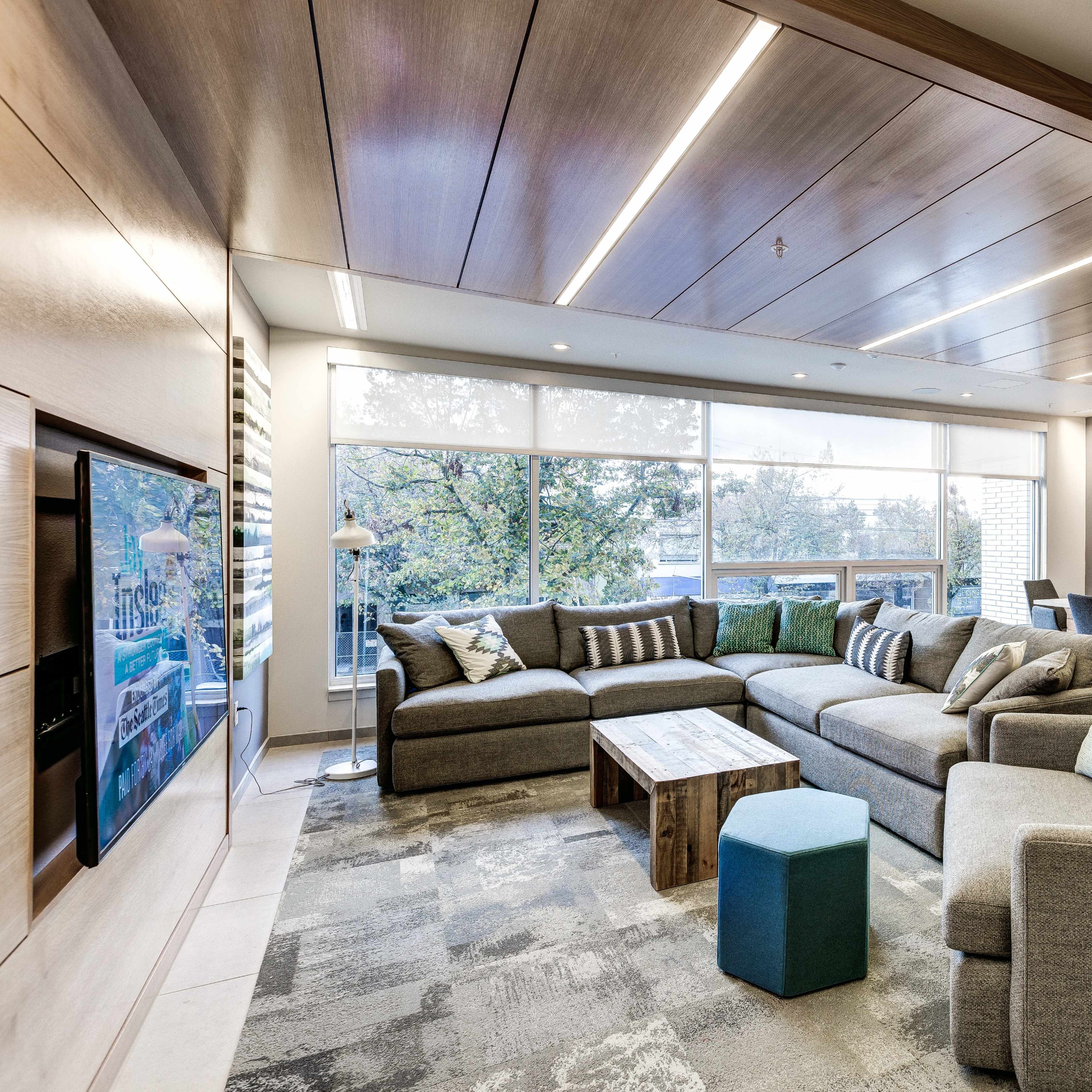 A modern living room with a large sectional sofa, a coffee table, and a dining area in the background, featuring natural light from large windows.