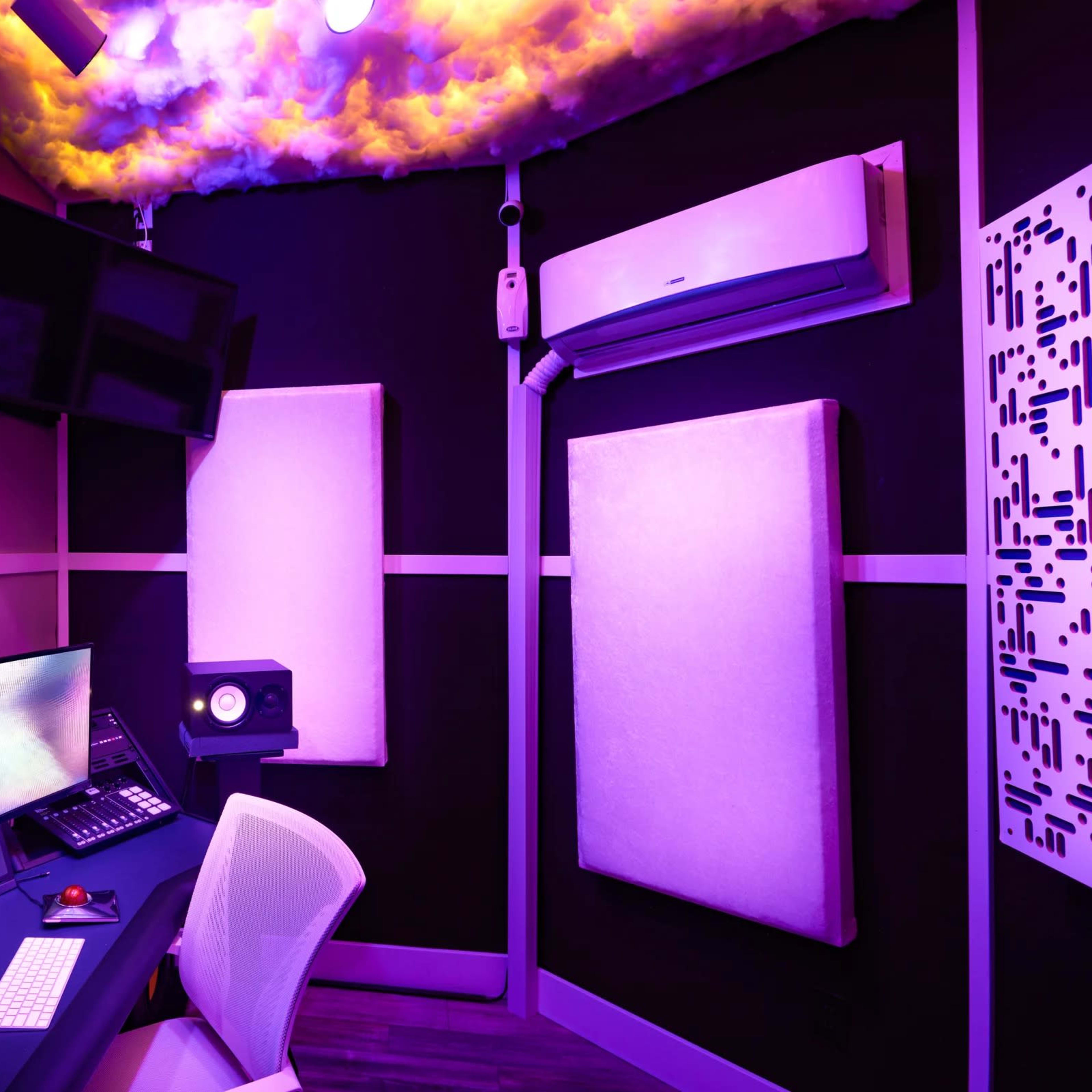A modern music studio with multiple screens, sound panels, and colorful lighting.