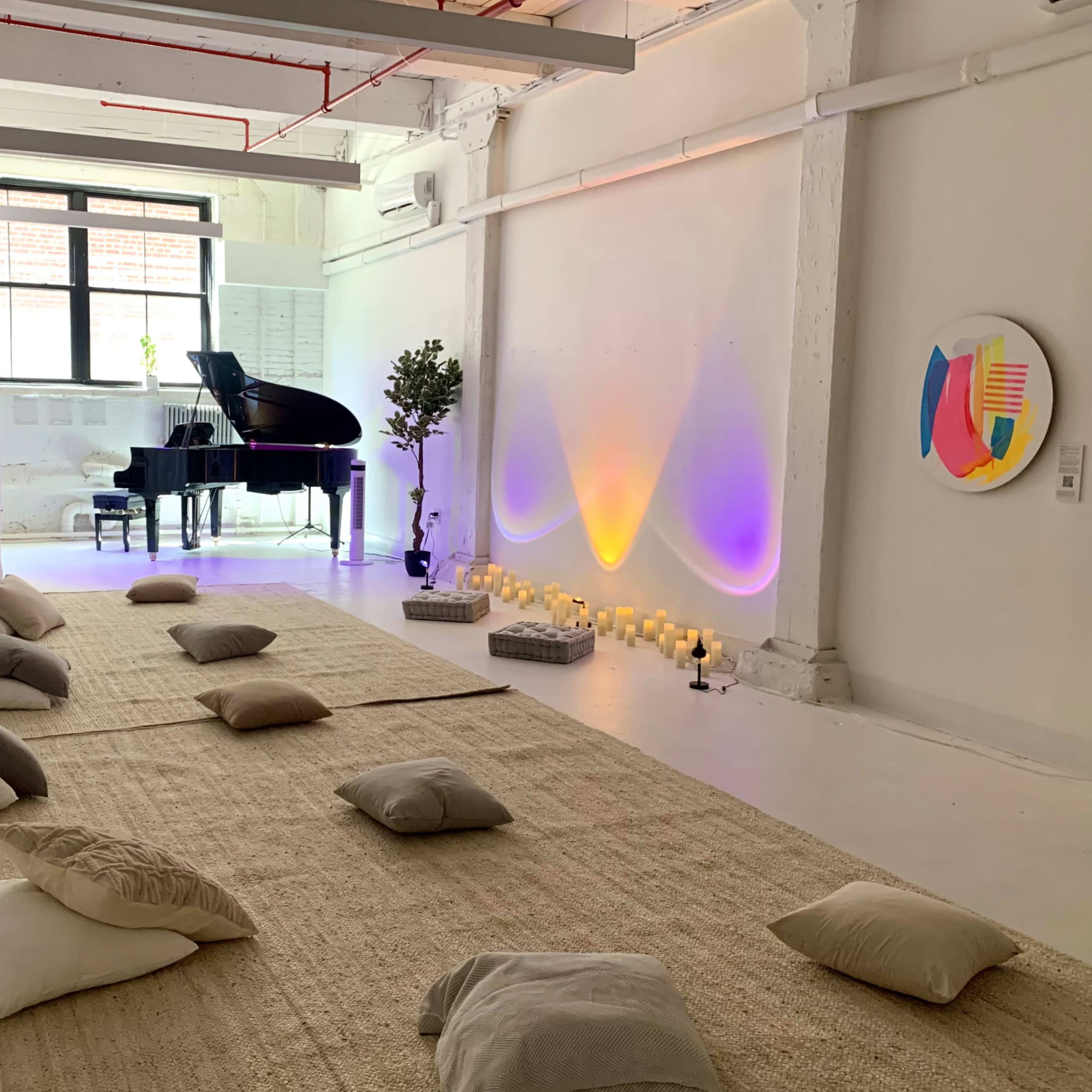 A spacious, minimalistic room with a grand piano, cushions arranged on a natural fiber rug, and soft lighting enhanced by colorful glow effects and candles along the walls.