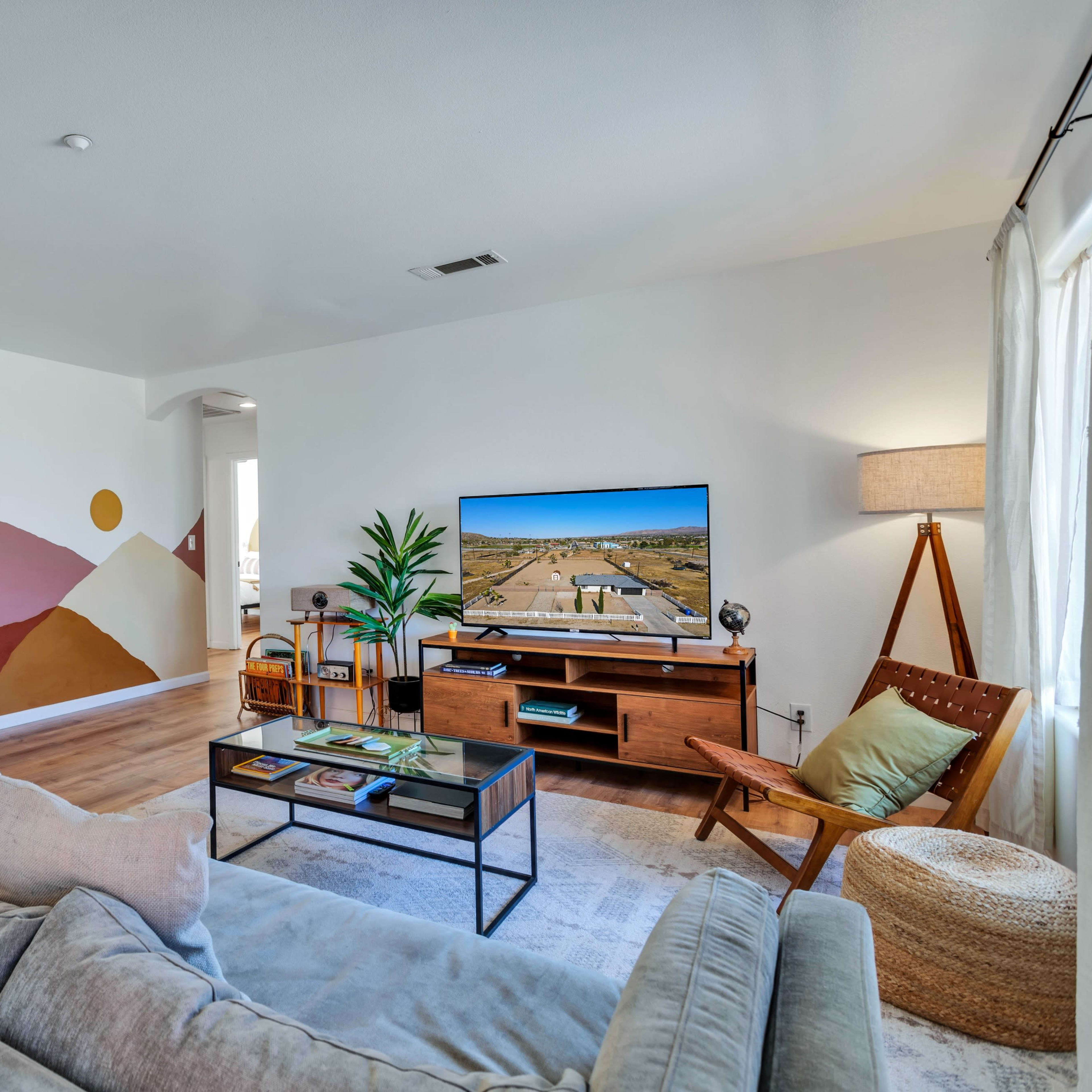 A living room features a modern couch, a television on a wooden console, and a mural of mountains and celestial shapes on one wall.