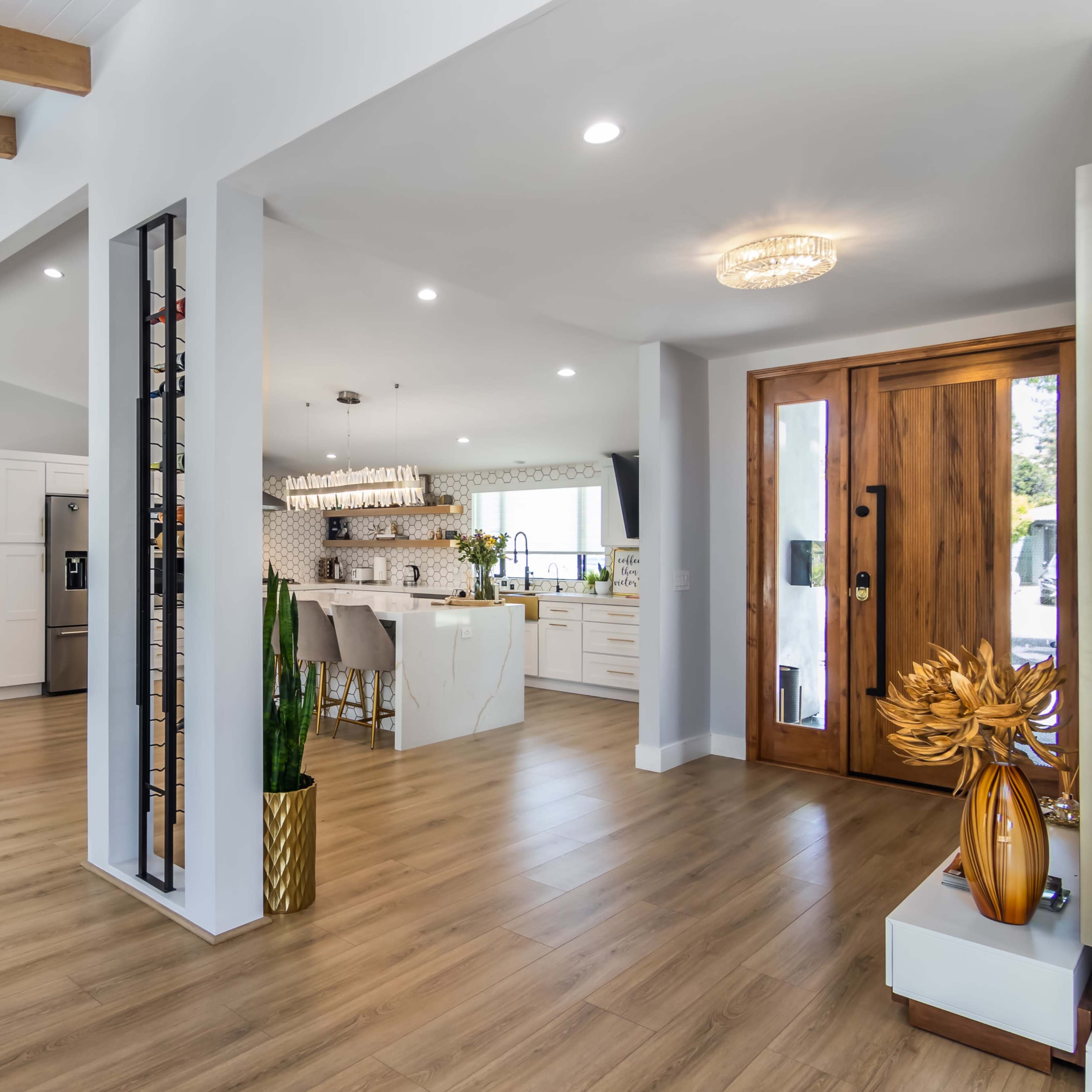A modern interior with an open floor plan, featuring a living area with a couch, a kitchen with a bar seating area, and a front door with large glass panels.