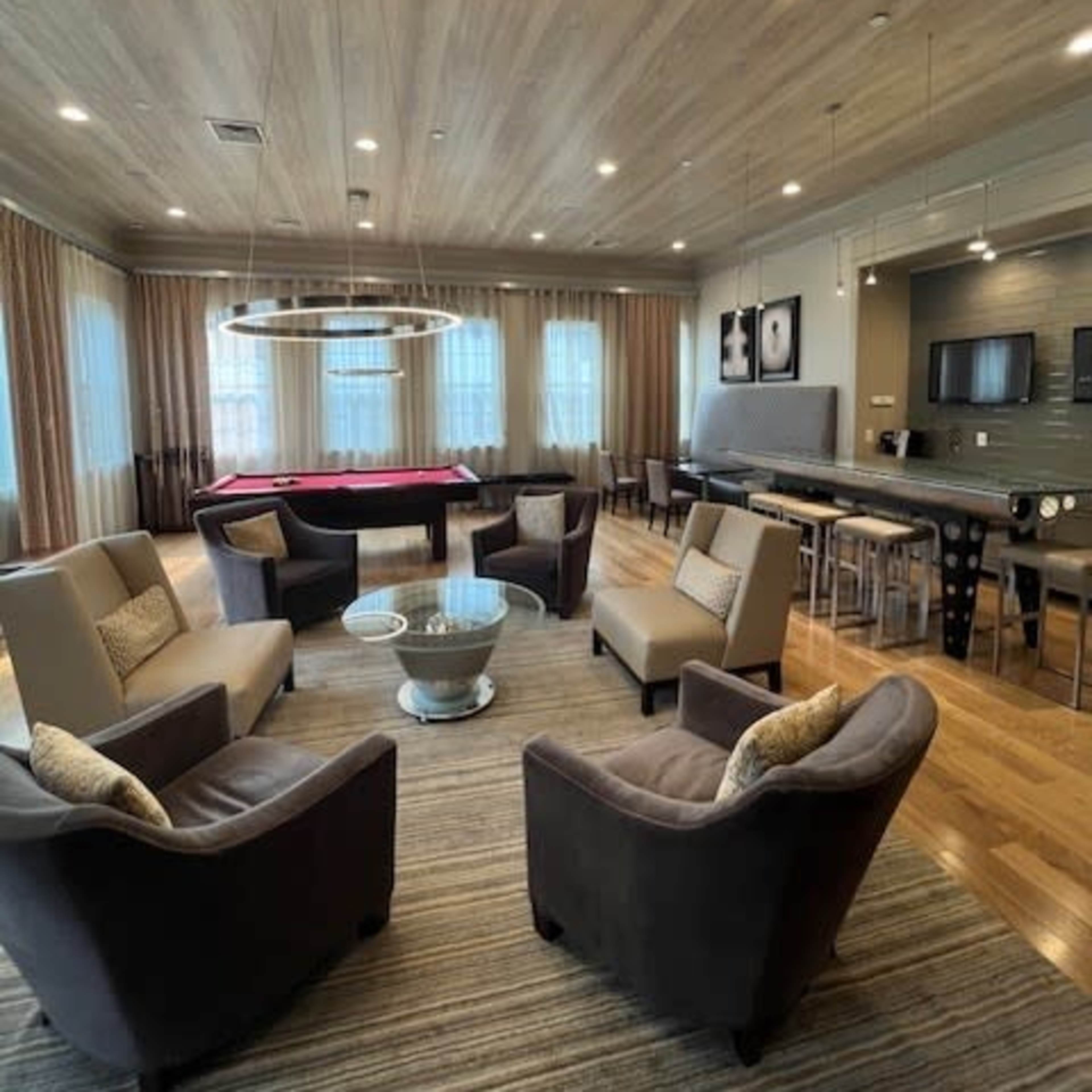 A spacious lounge area features four armchairs arranged around a coffee table, with a pool table and dining area in the background.