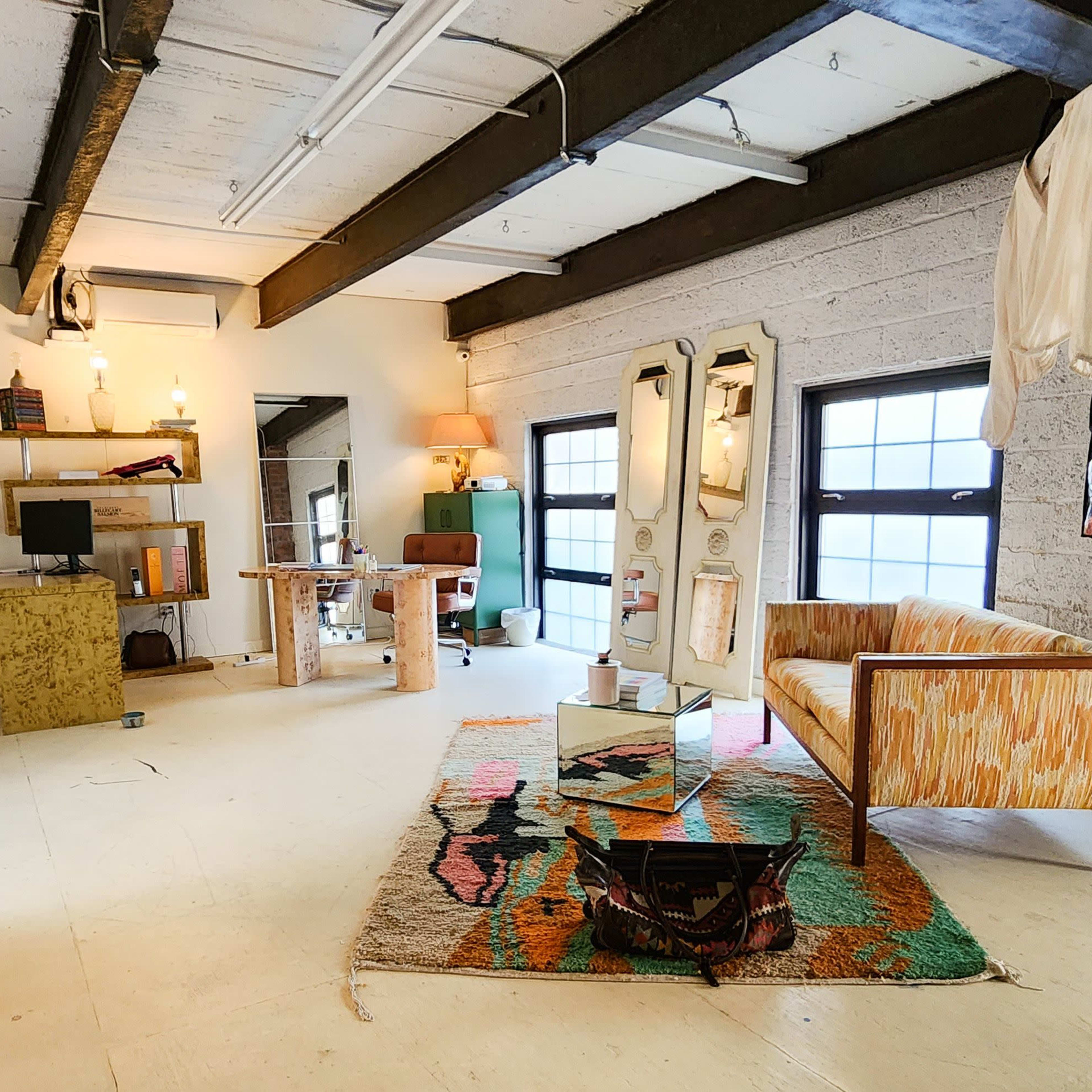 A spacious loft-style room with a seating area, a desk, and a large window, featuring a mix of modern and vintage decor.