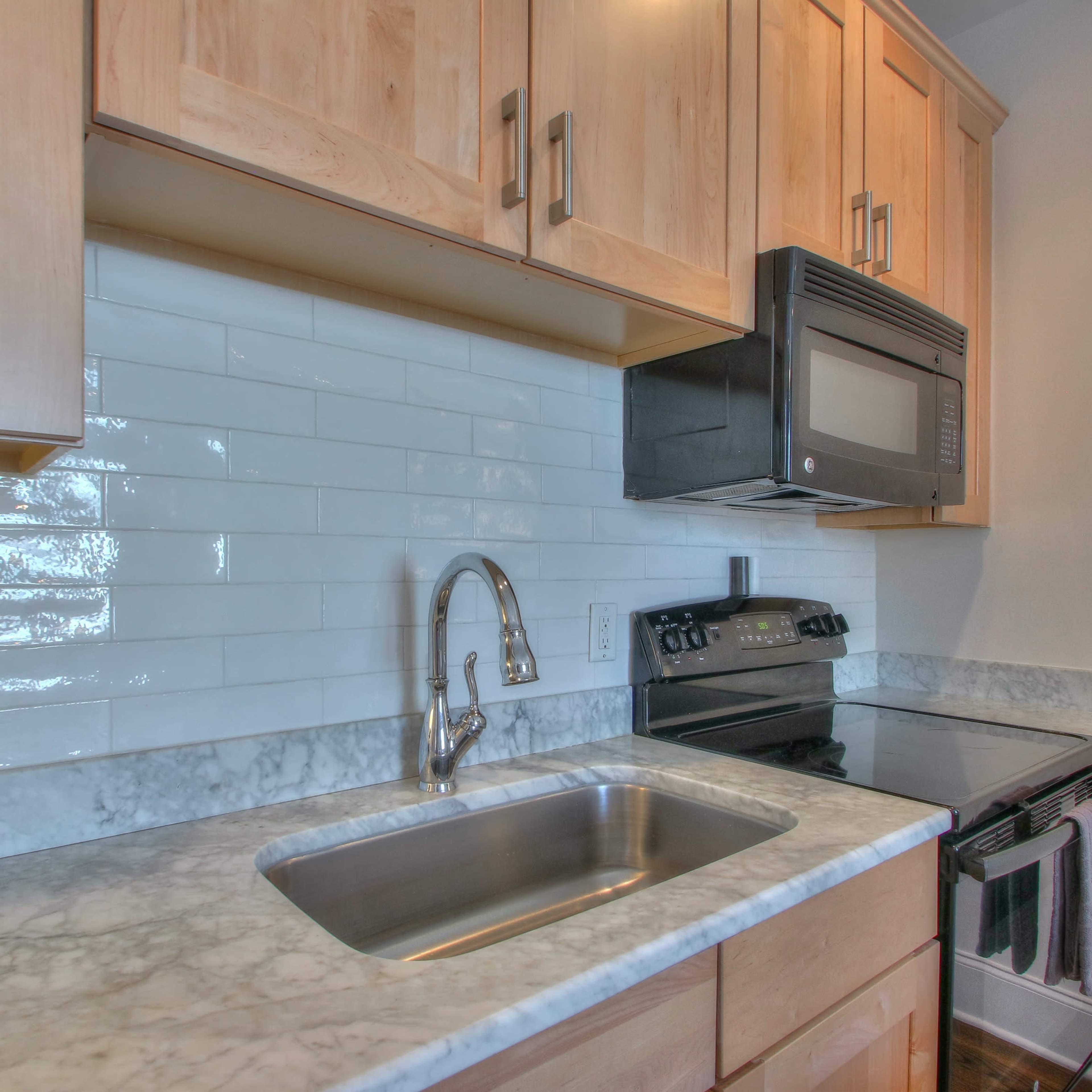A kitchen with wooden cabinets, a marble countertop, a stainless steel sink, and a black microwave and oven built into the cabinetry.