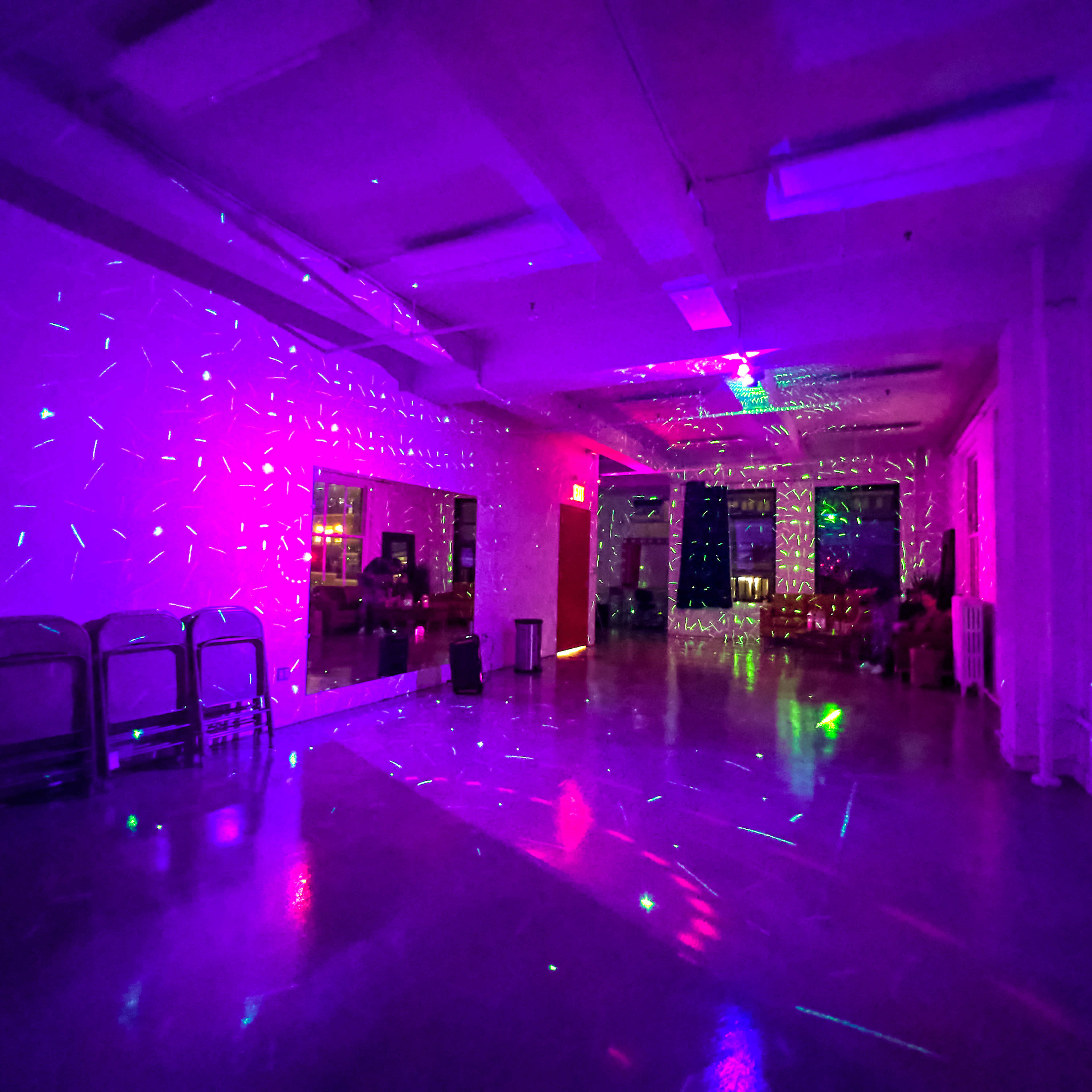 A spacious room lit with colorful laser lights reflecting on the walls and floor.