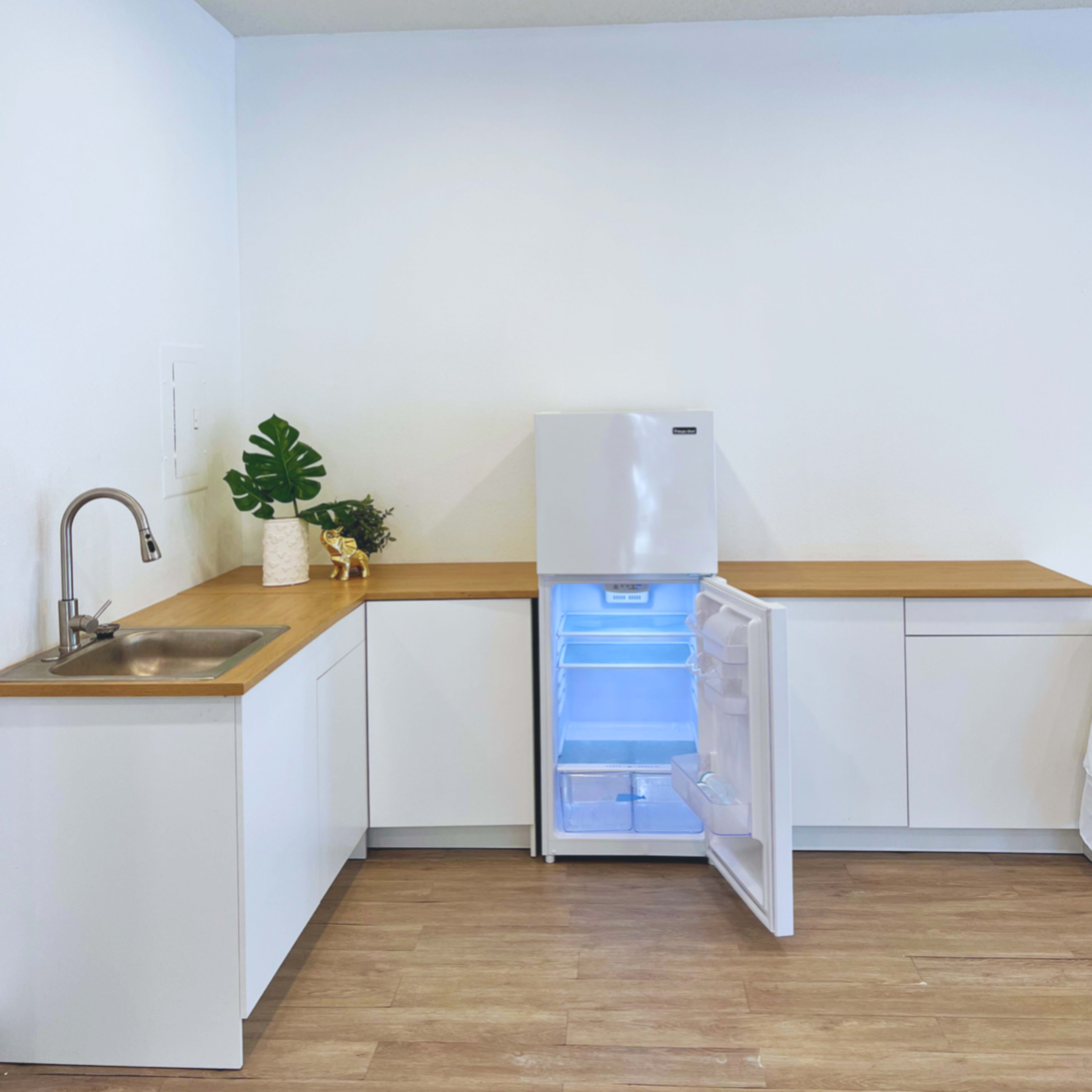 A modern kitchen with white cabinets, a stainless steel sink, and an open refrigerator displaying a bright interior.