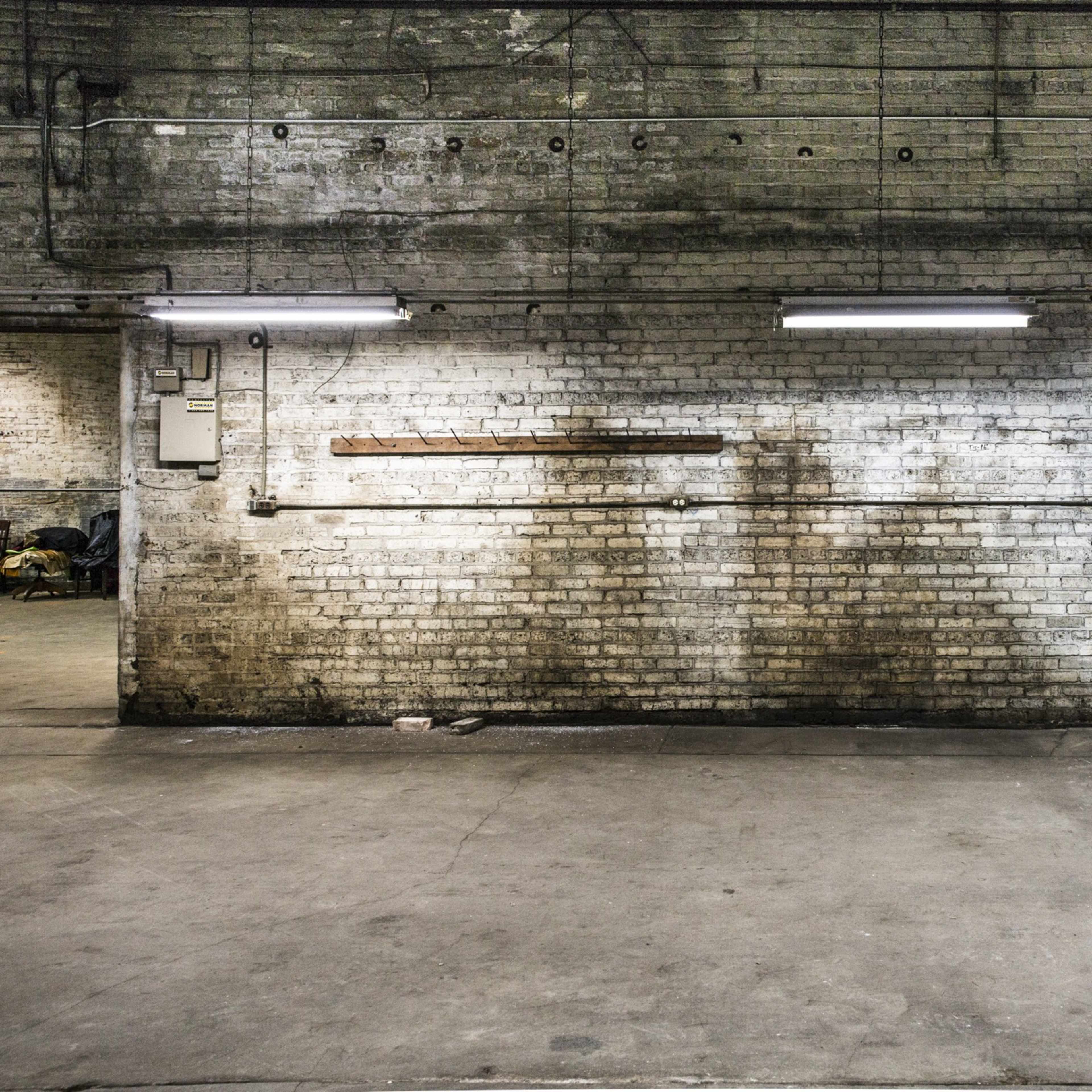 A large, empty industrial space with a brick wall, overhead lights, and a concrete floor.