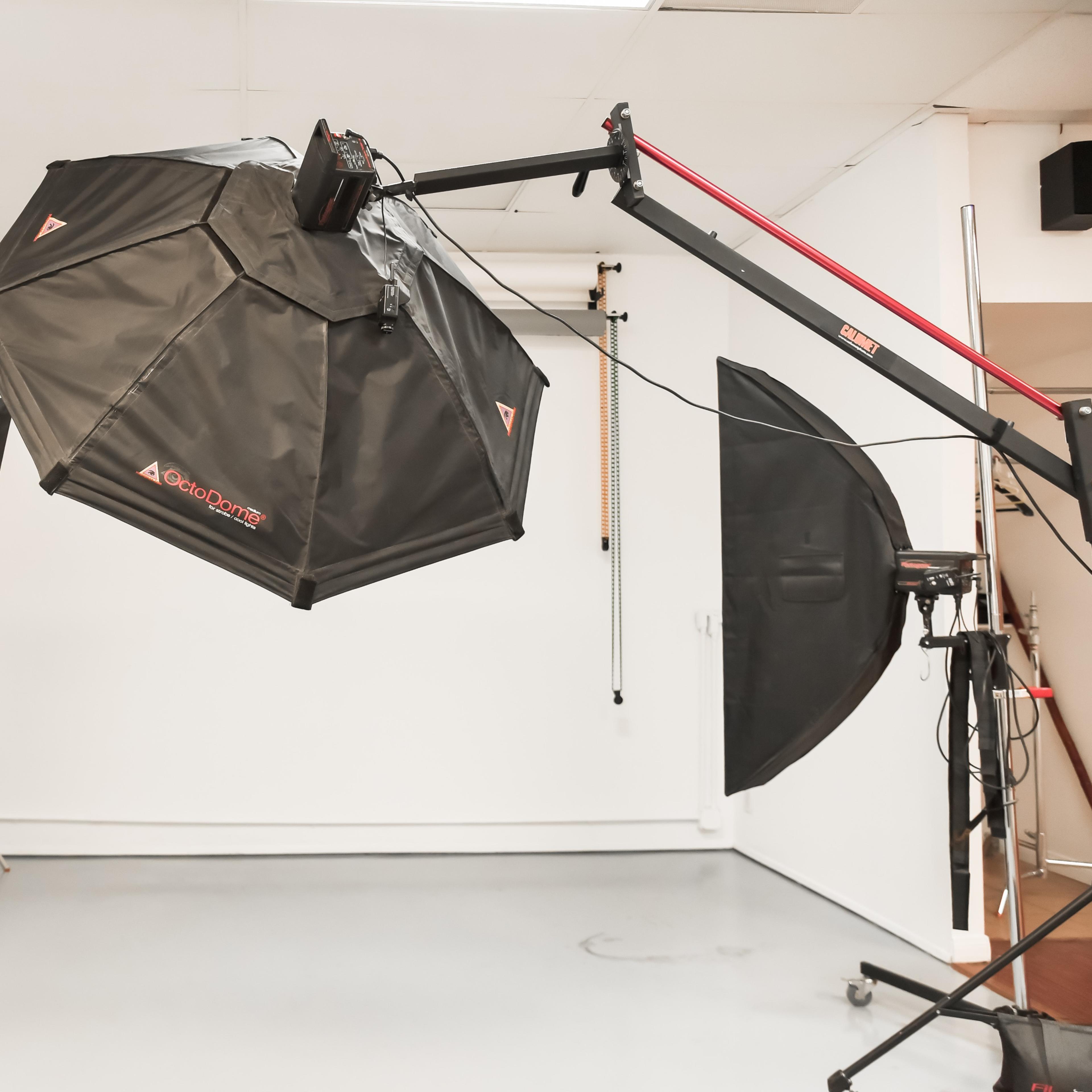 A large octagonal softbox with light stands is set up in a spacious photography studio with a blank wall.