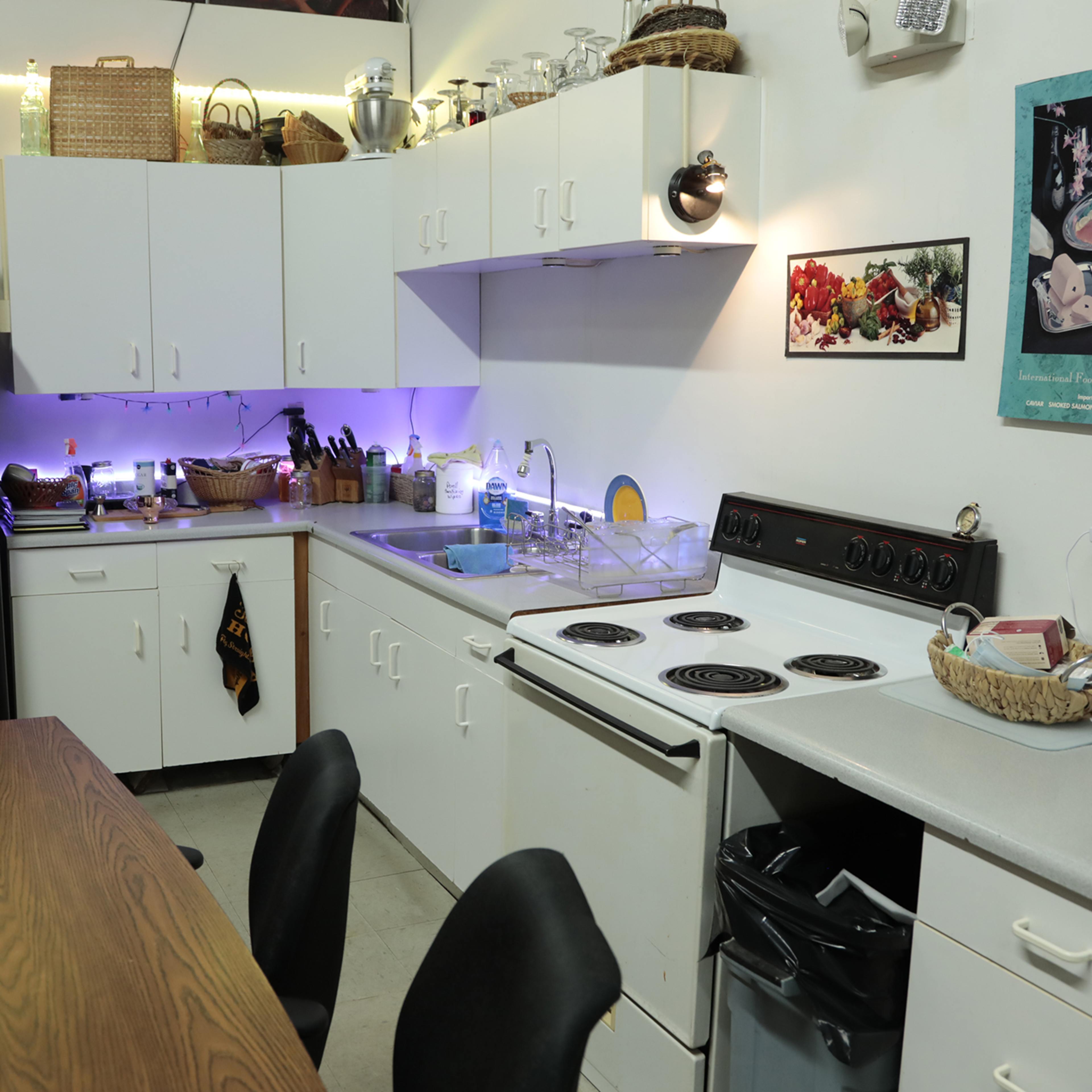 A kitchen with white cabinets, a stove, and a dining table, featuring various items on the counters and shelves.