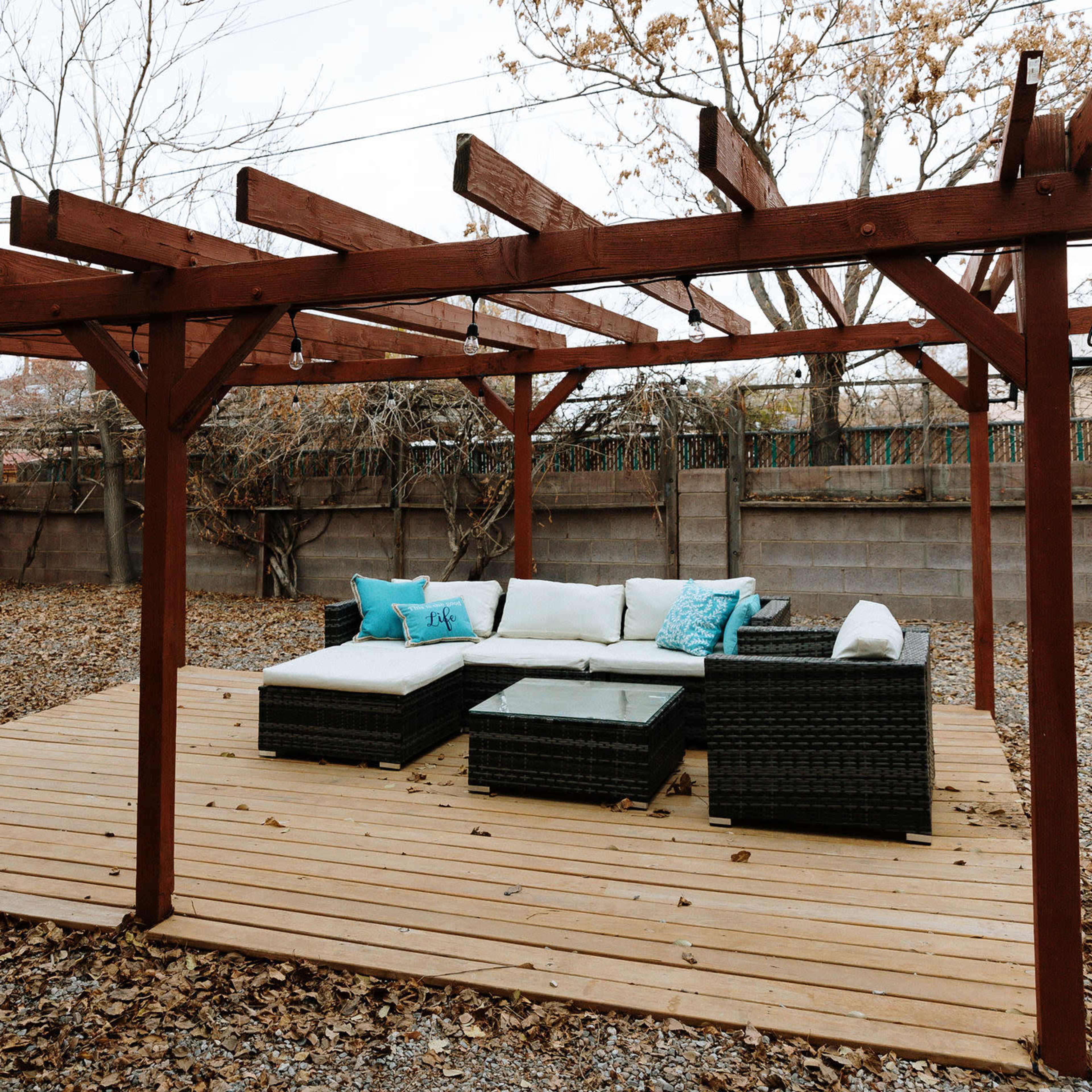 A wooden patio structure with a seating area consisting of a low table and sofas placed on a gravel surface.