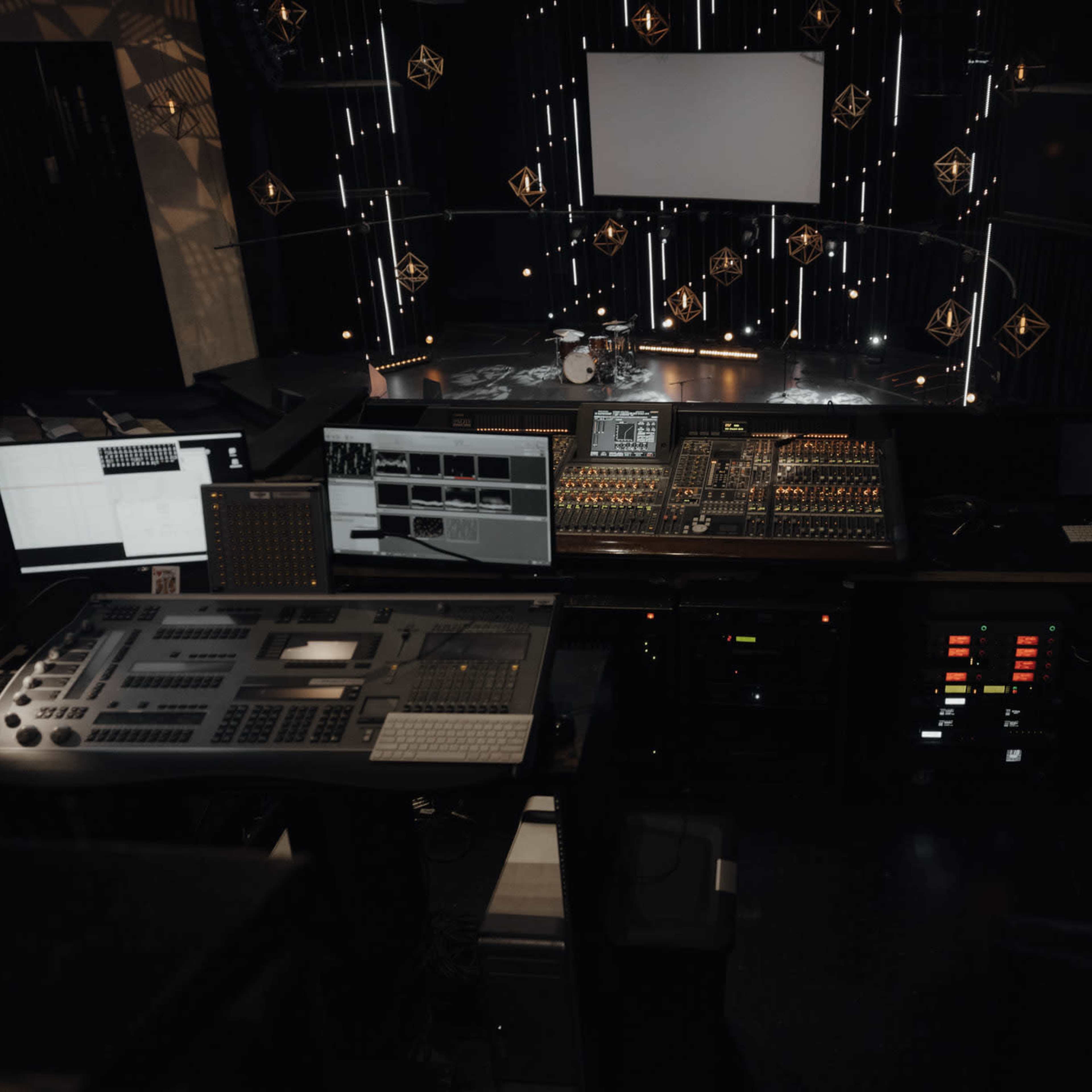 A sound and lighting control room with various screens and equipment in front of a performance stage.