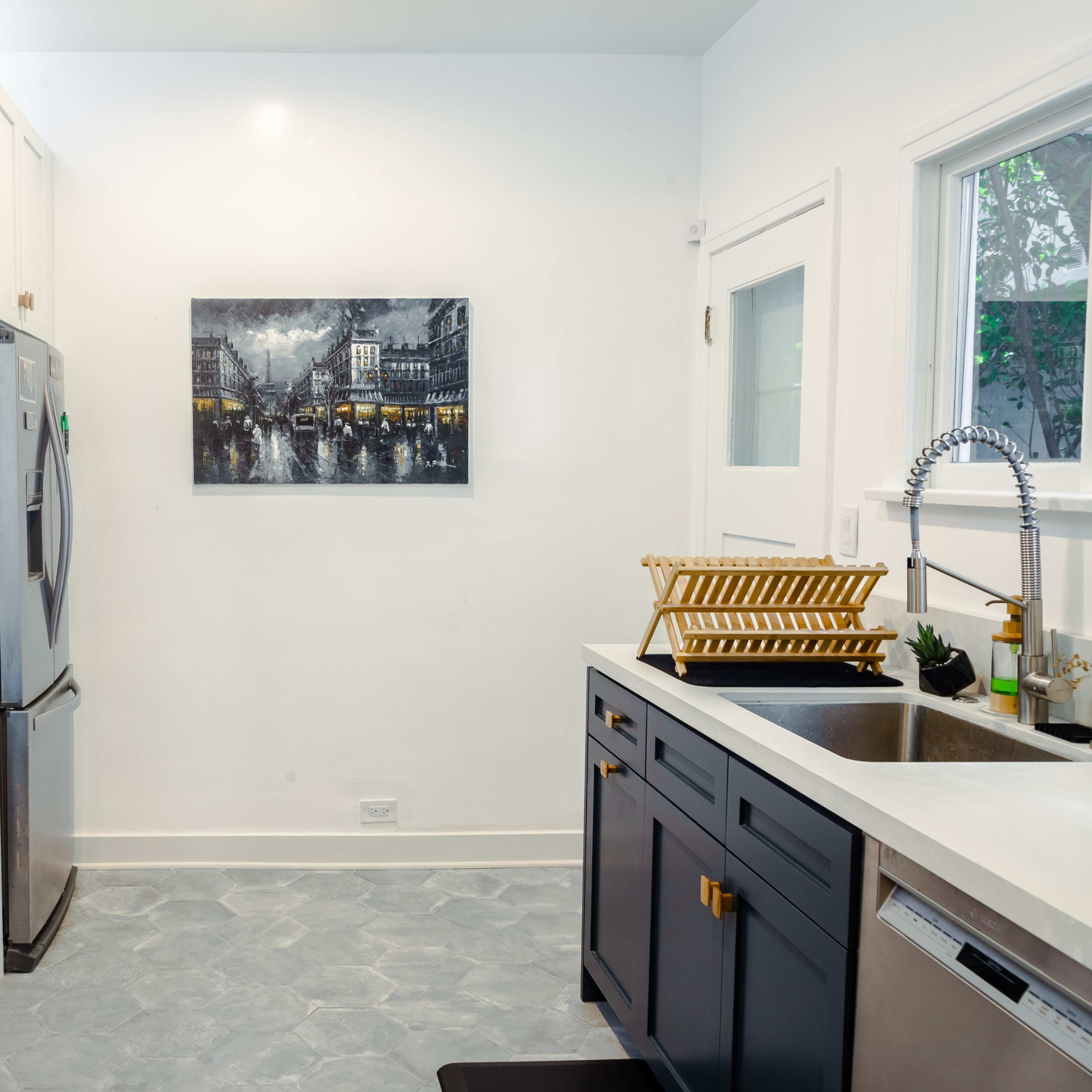 A modern kitchen features stainless steel appliances, dark cabinetry, and a wall-mounted black-and-white cityscape photograph.