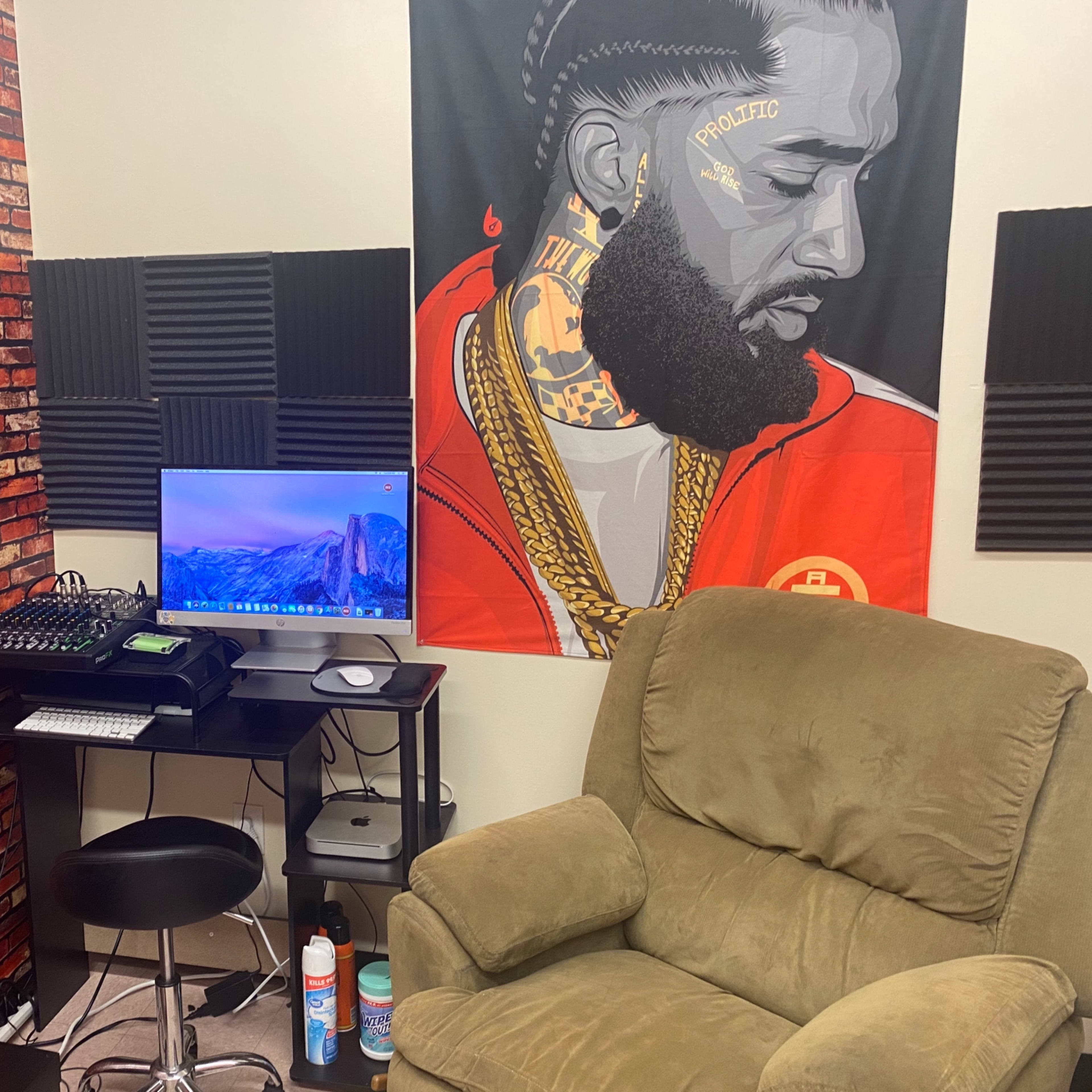 A small room featuring a desk with a computer monitor, a green armchair, and a wall adorned with a mural of a man and a brick pattern.