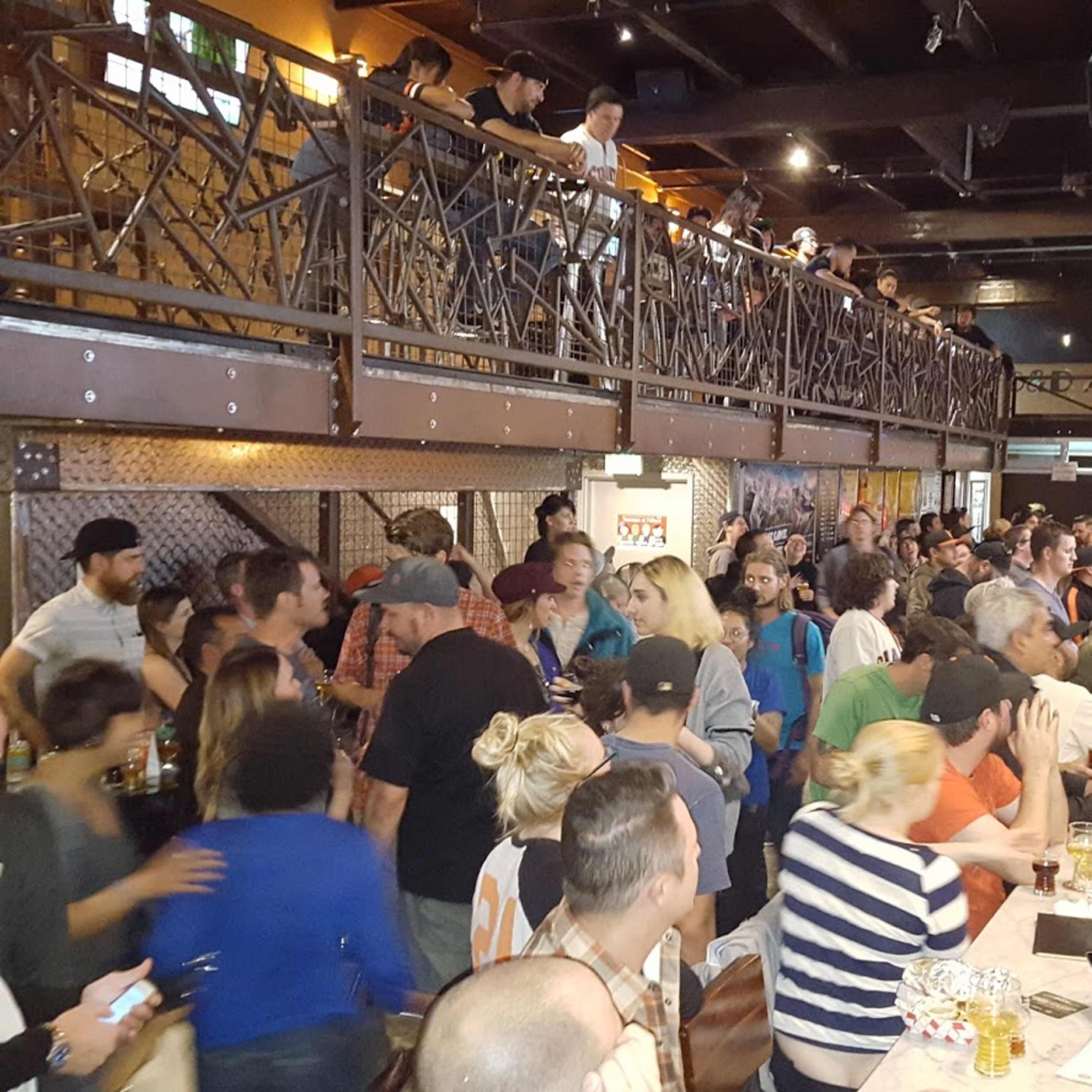 A crowded bar scene shows patrons mingling and socializing at tables and along the bar, with a second level visible in the background.