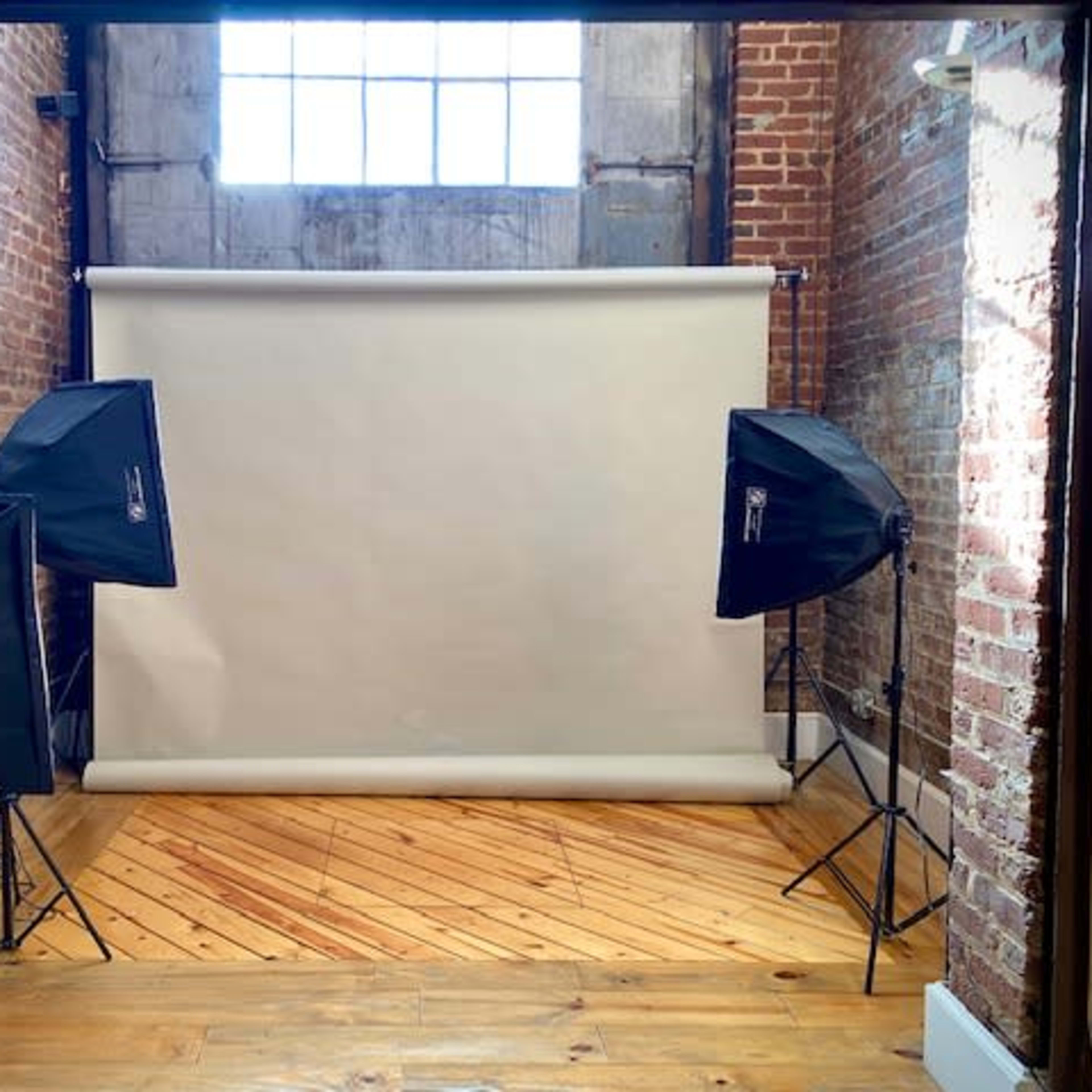 A photography studio setup with three softbox lights surrounding a blank backdrop.
