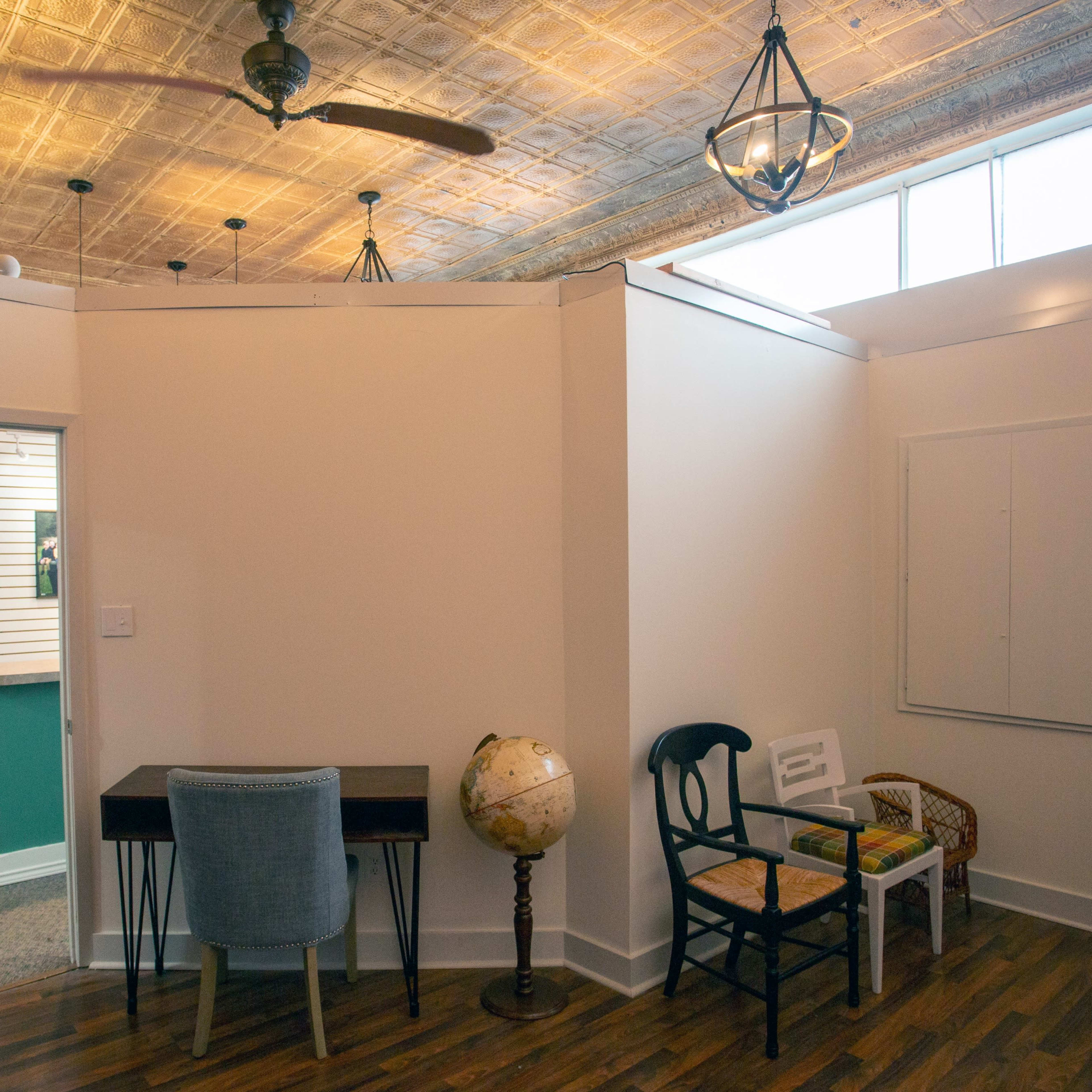 A well-lit room featuring a wooden floor, a globe, a desk with a chair, and an entryway leading to another space with a slatted wall.