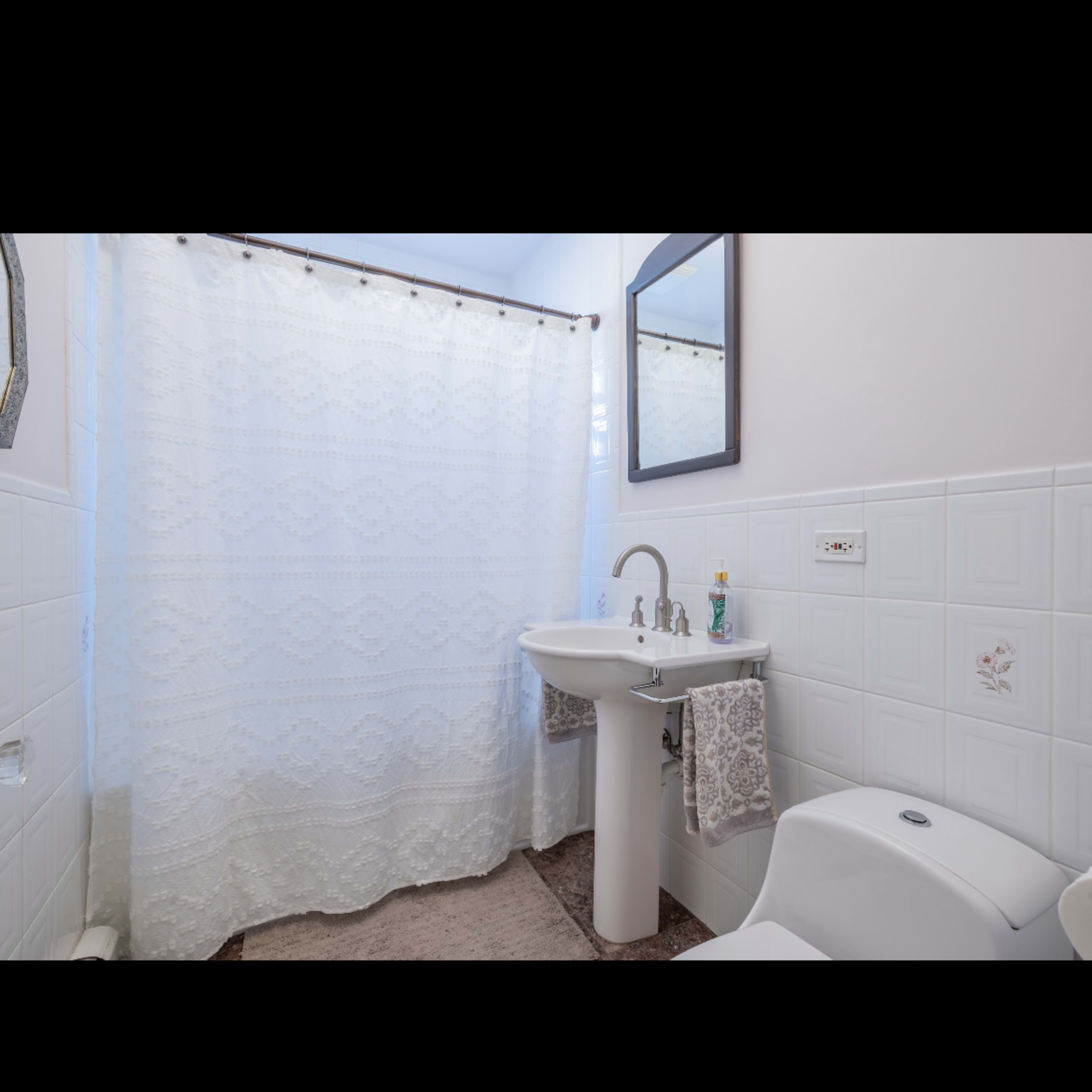 A bathroom featuring a shower curtain, a pedestal sink, and a toilet against tiled walls.