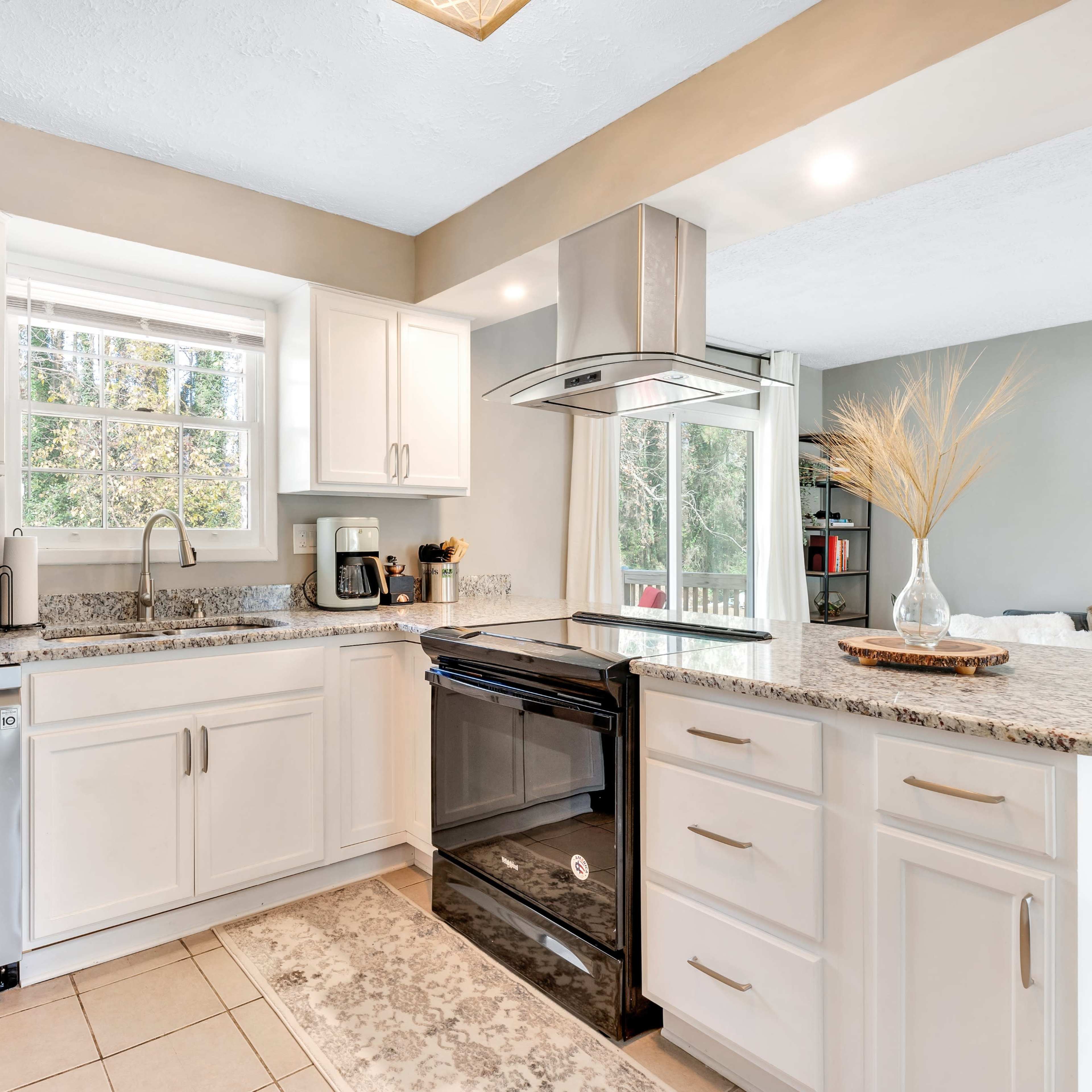 A modern kitchen with white cabinets, stainless steel appliances, and a window overlooking a garden area.