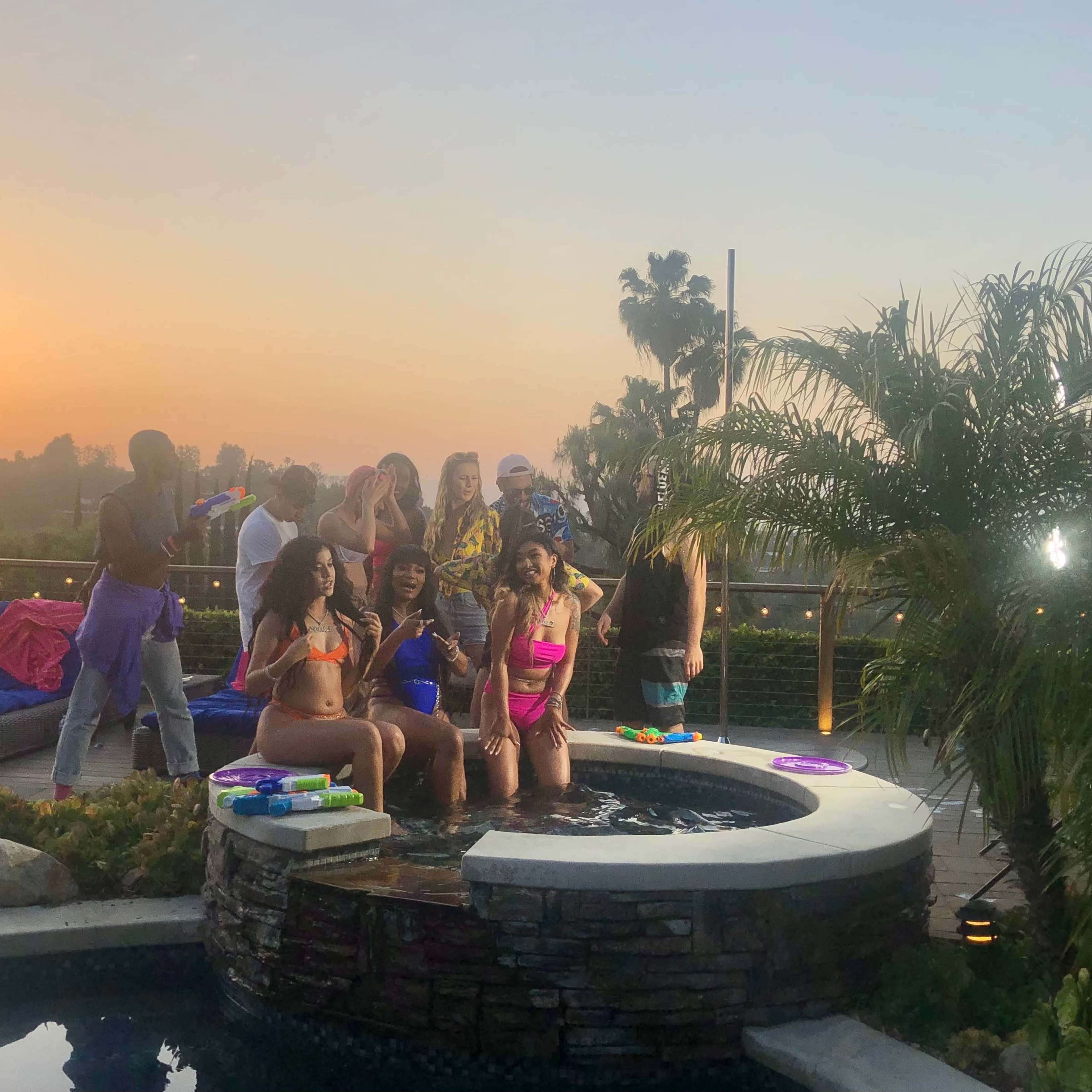 A group of people poses by a hot tub during sunset, with some holding water guns.