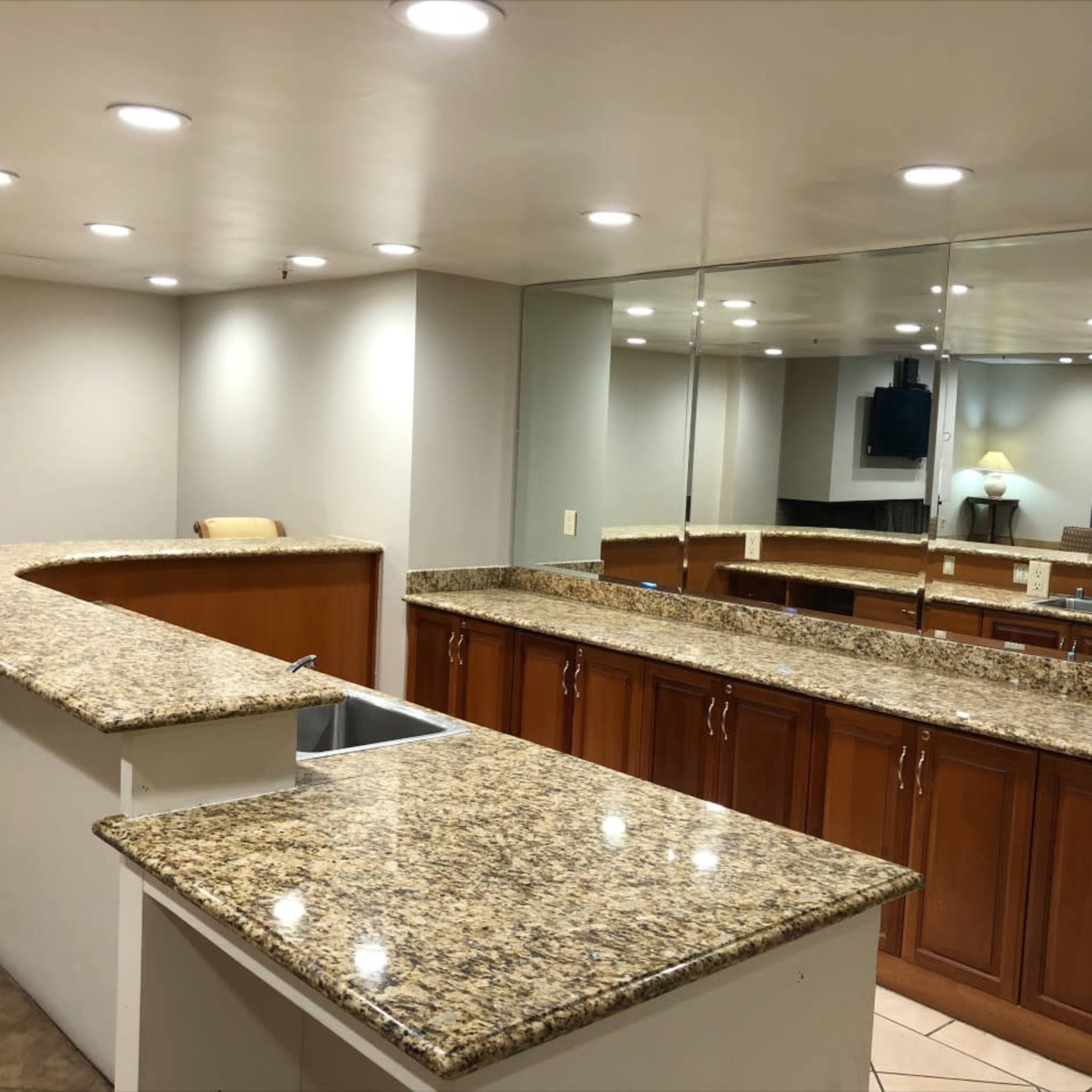 A spacious room with a curved granite countertop, wooden cabinetry, and a mirrored wall reflecting the space.