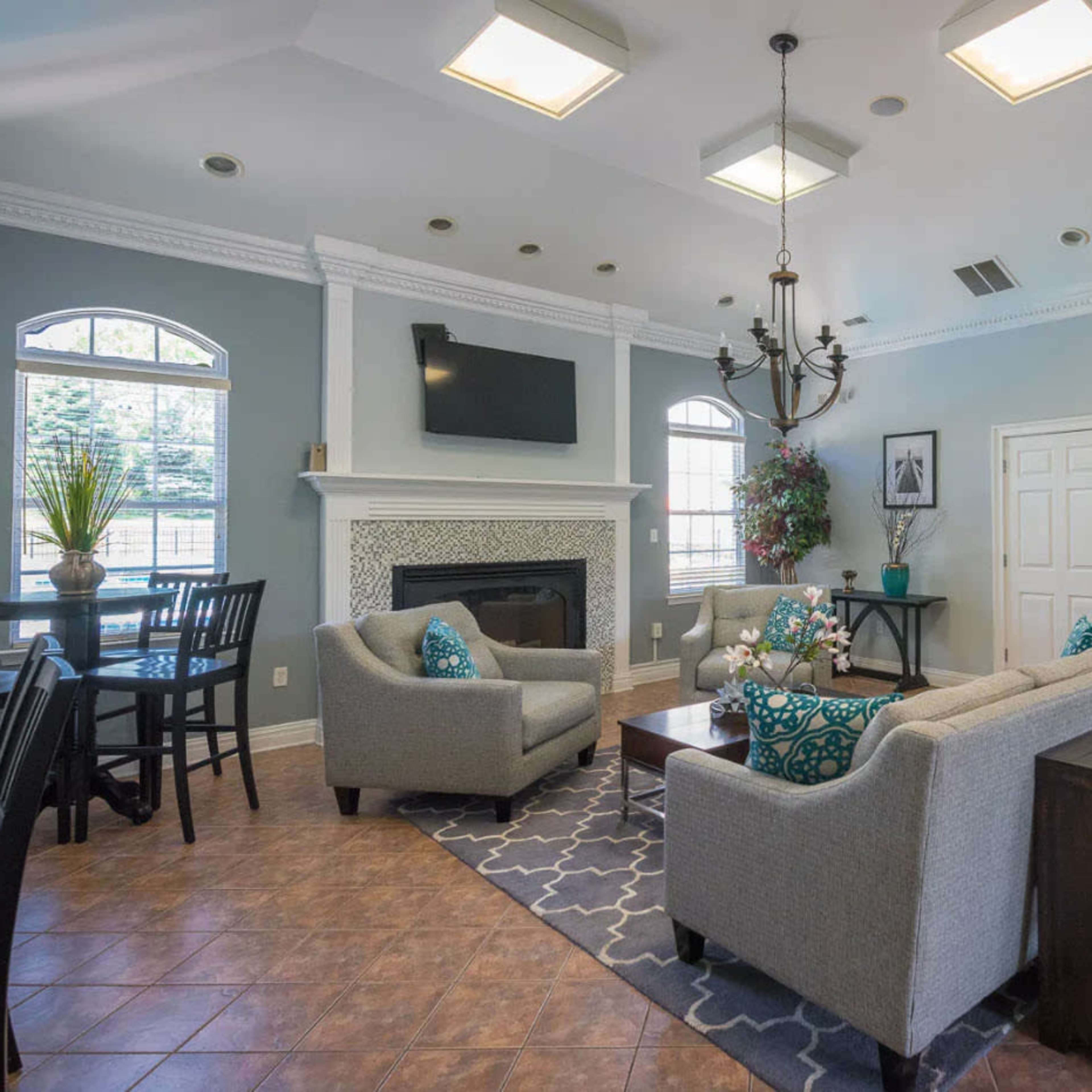 A well-lit lounge area featuring two gray armchairs, a coffee table, and a fireplace, with dining tables and chairs positioned along the sides.