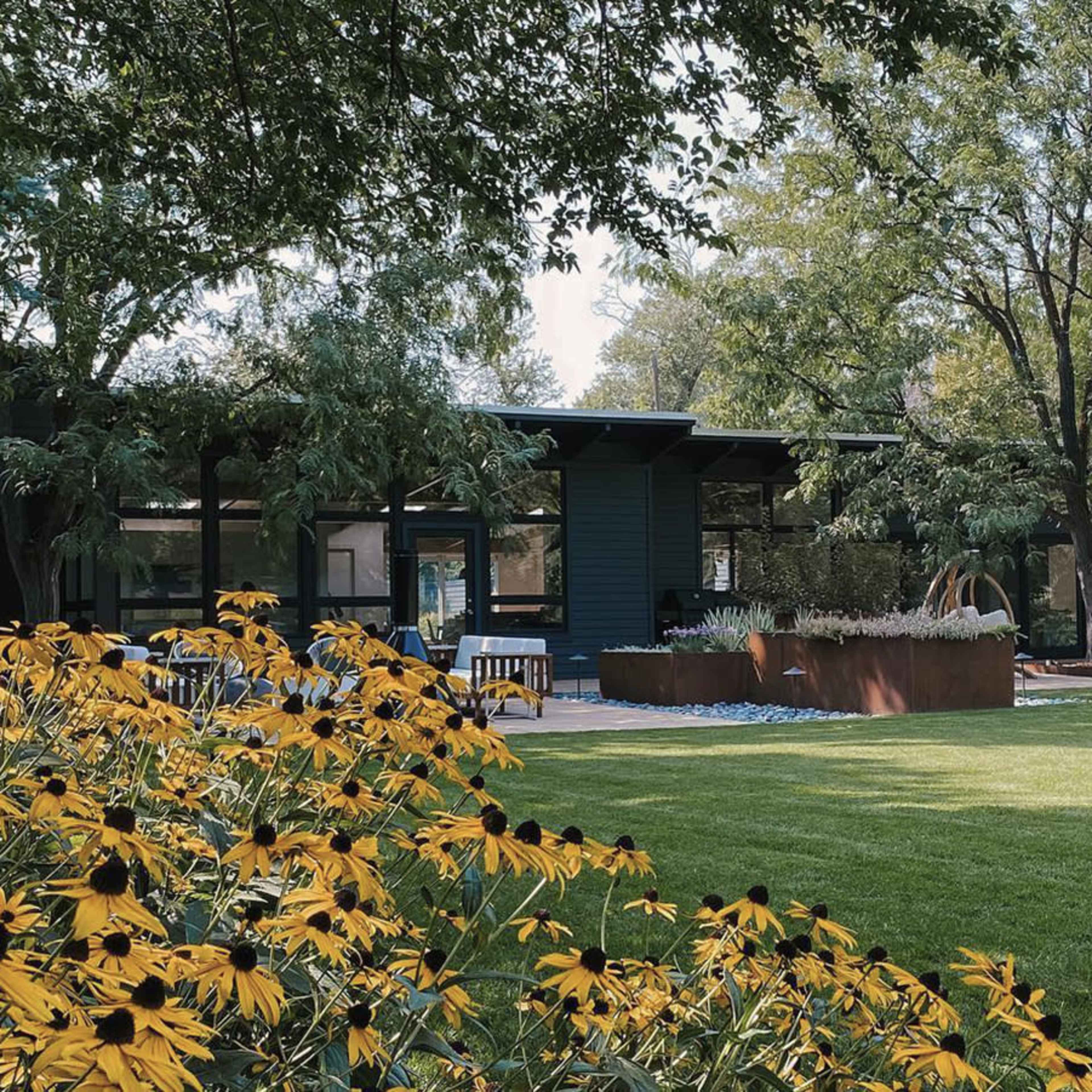 A modern house with large windows is surrounded by greenery and colorful flowers on a well-maintained lawn.