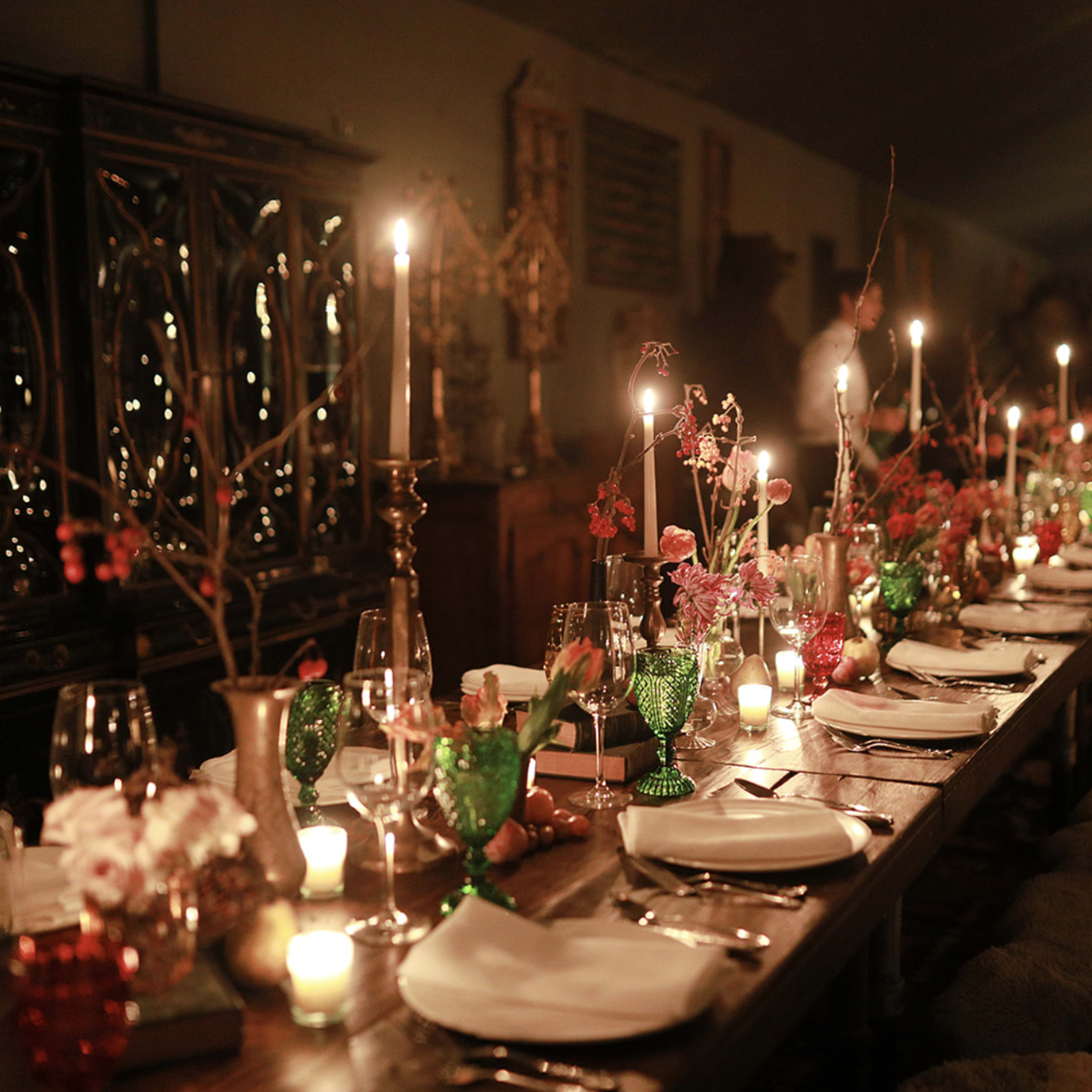 A long dining table is elegantly set with candles, glassware, and floral arrangements in a dimly lit room.