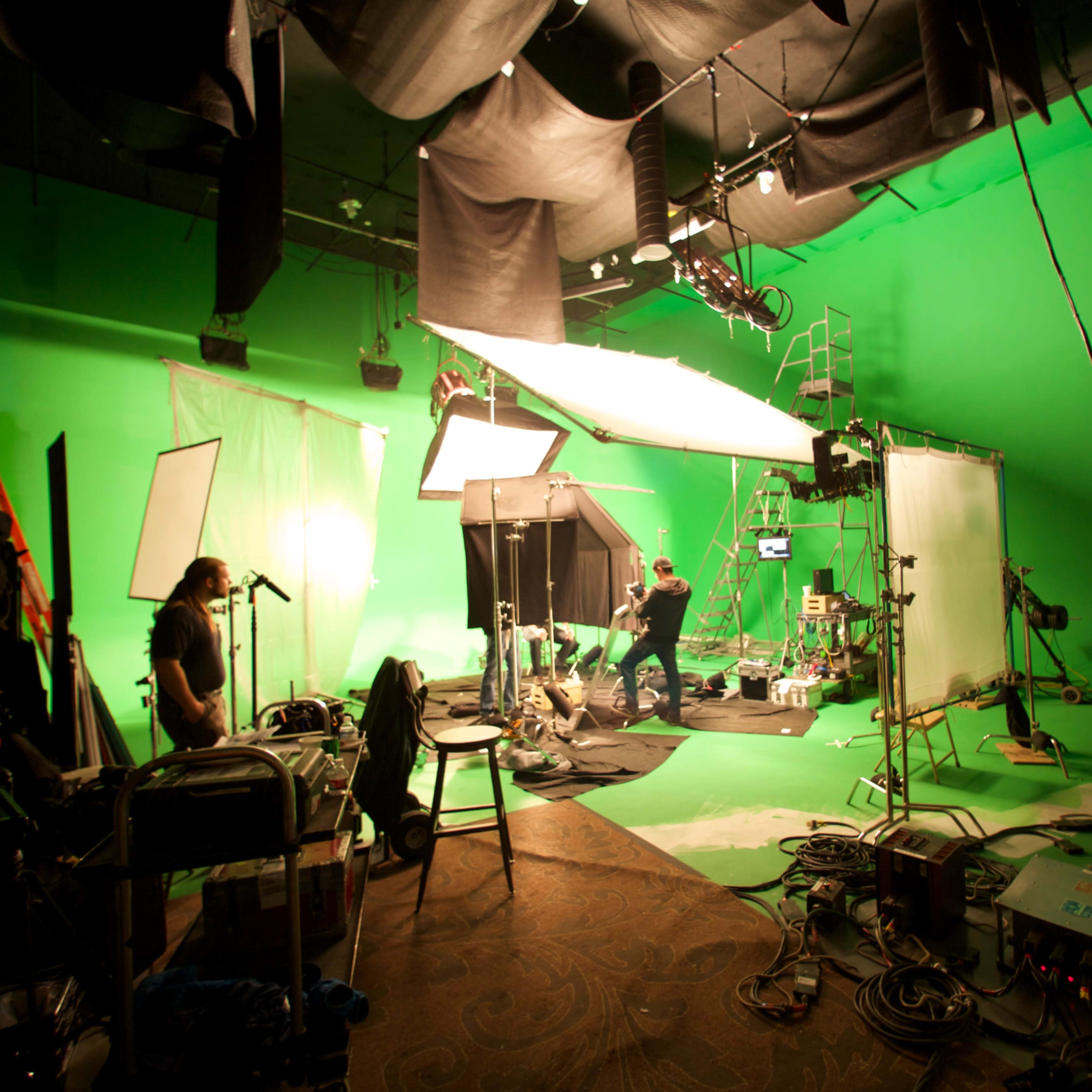 A film studio scene shows crew members setting up equipment on a green screen backdrop.