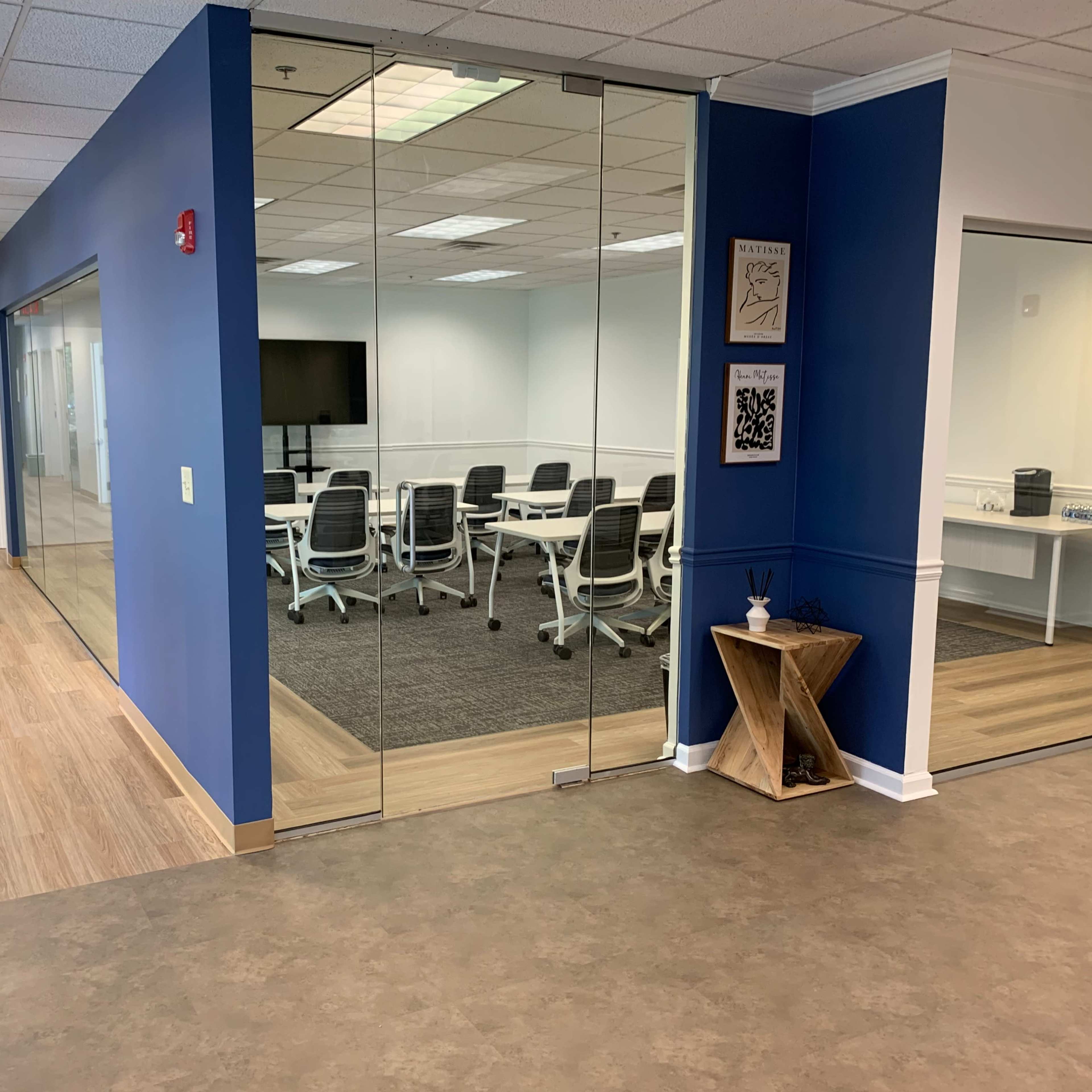 A modern office space with a blue accent wall, glass meeting room, and a hallway leading to other rooms.