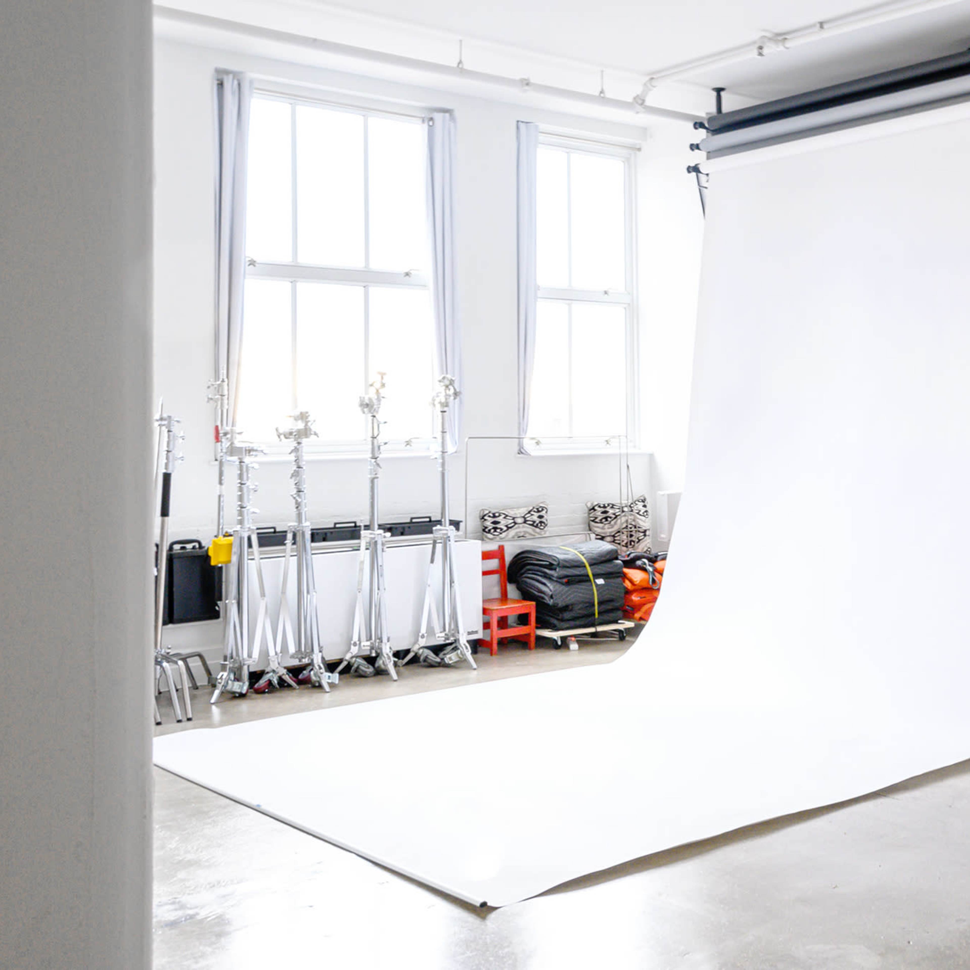 A photography studio with a large white backdrop, studio lighting equipment, and organized storage along the walls.