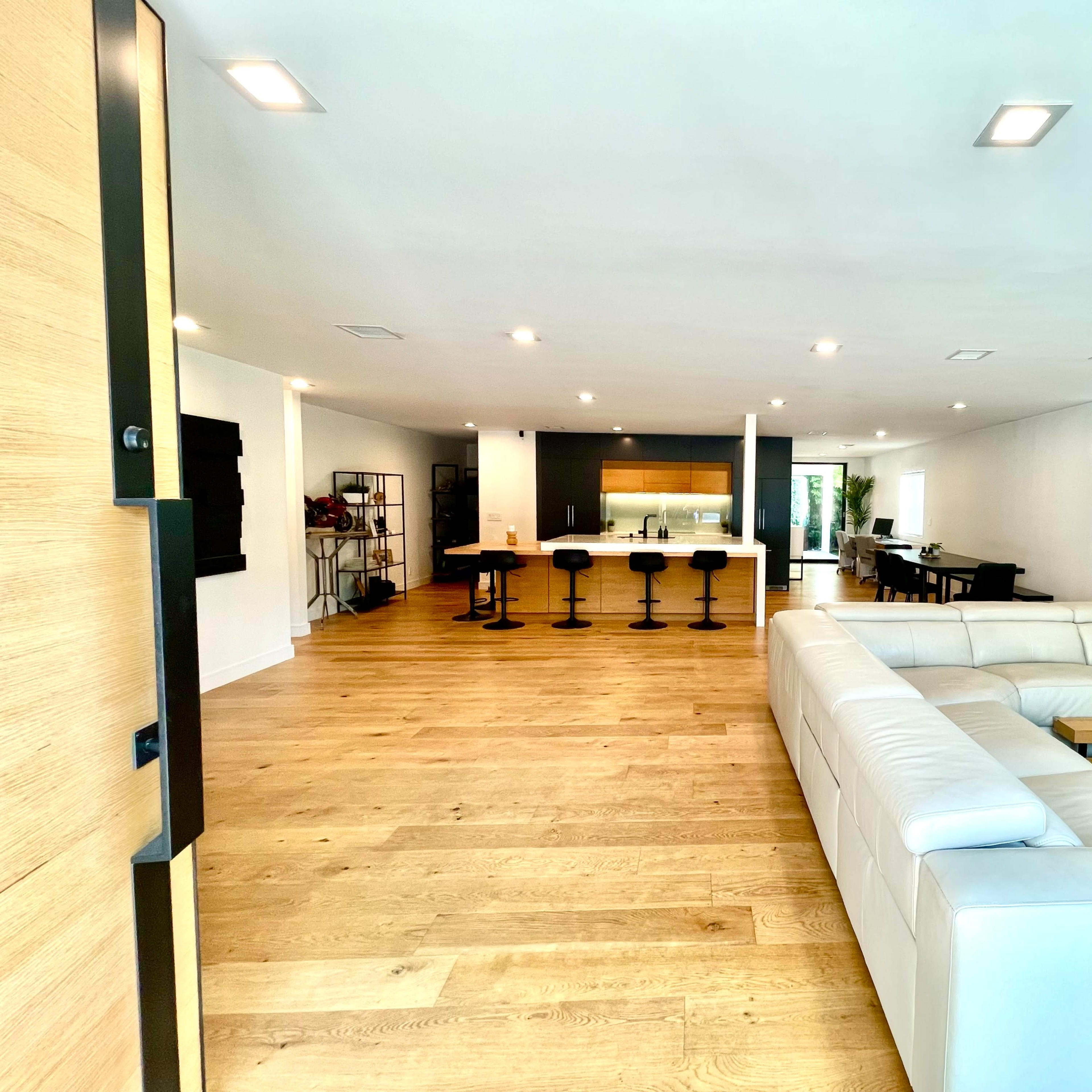 A spacious modern living area with a white sectional sofa facing a sleek kitchen and dining area.