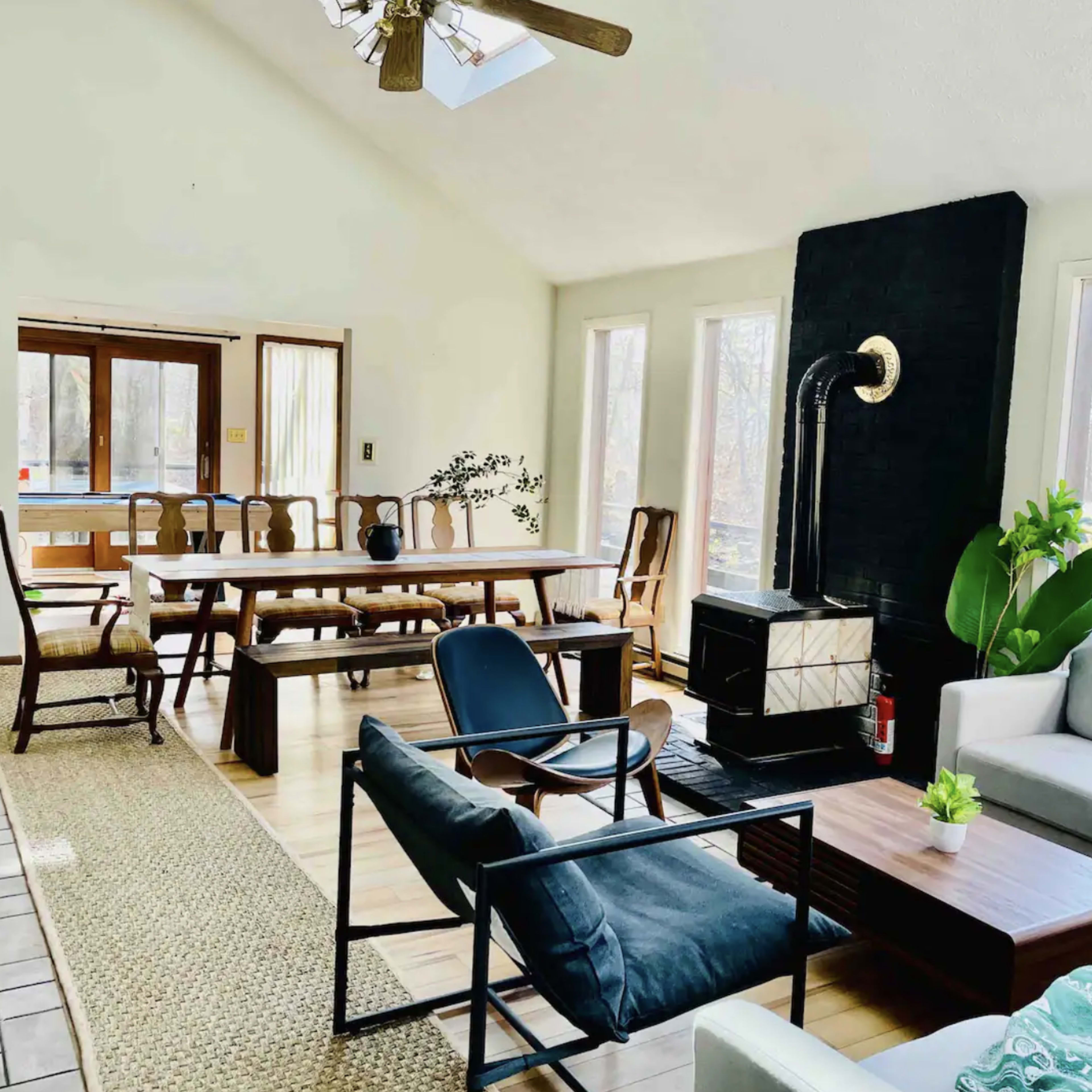 A spacious living area with a seating arrangement, a fireplace, and a long dining table surrounded by windows providing natural light.