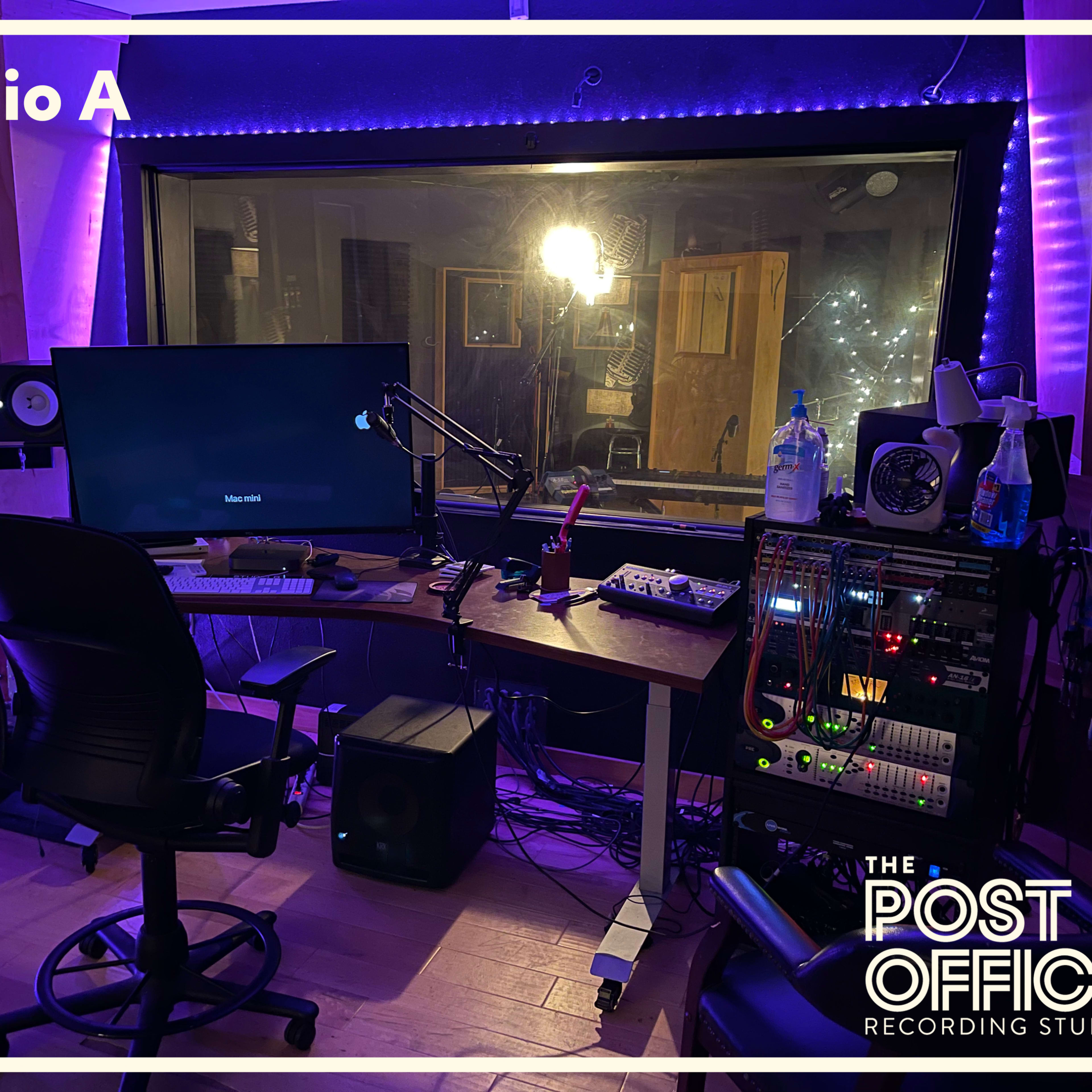 A recording studio with a desk, computer, and audio equipment, illuminated by purple LED lights.