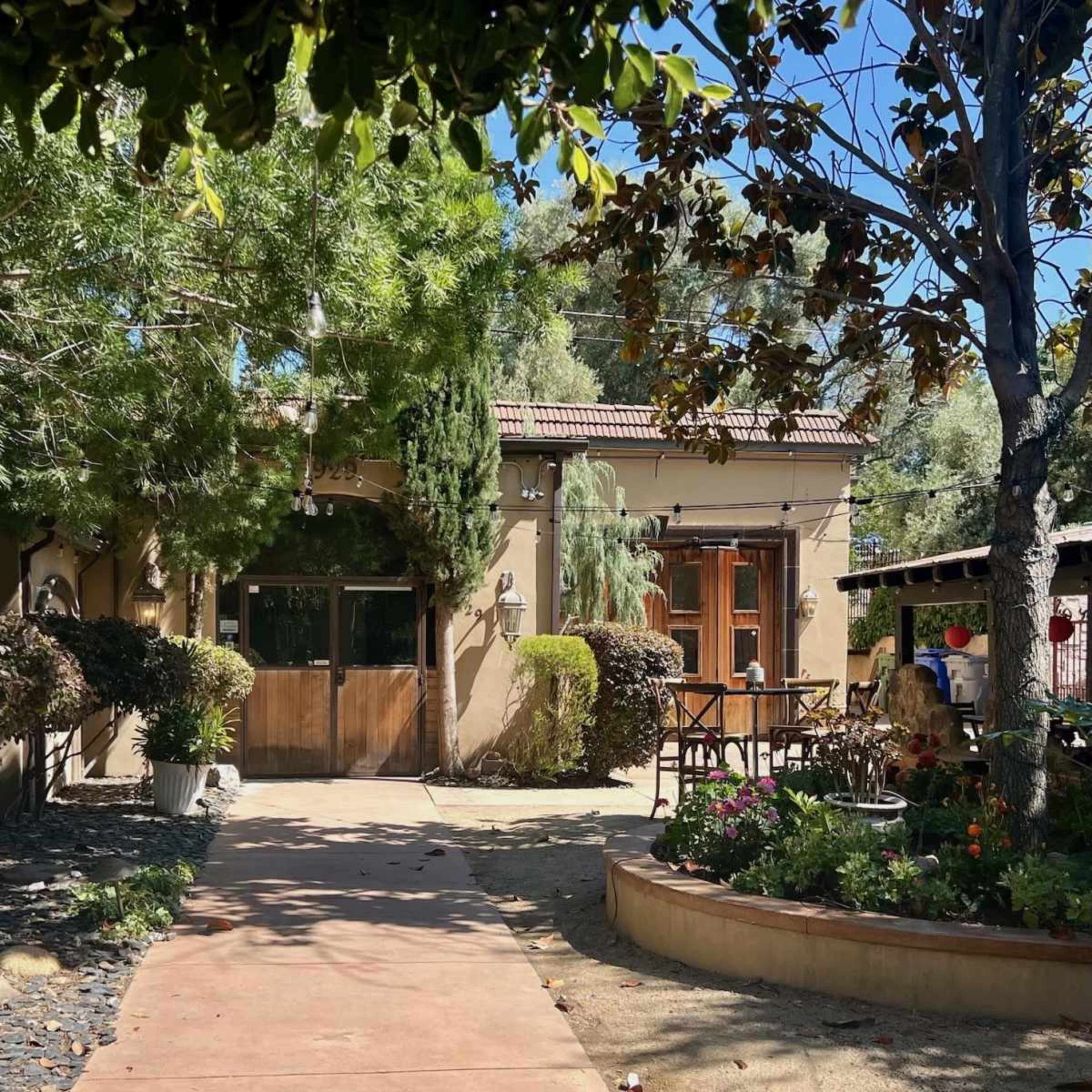 A pathway leading to a rustic building surrounded by greenery and outdoor seating areas.