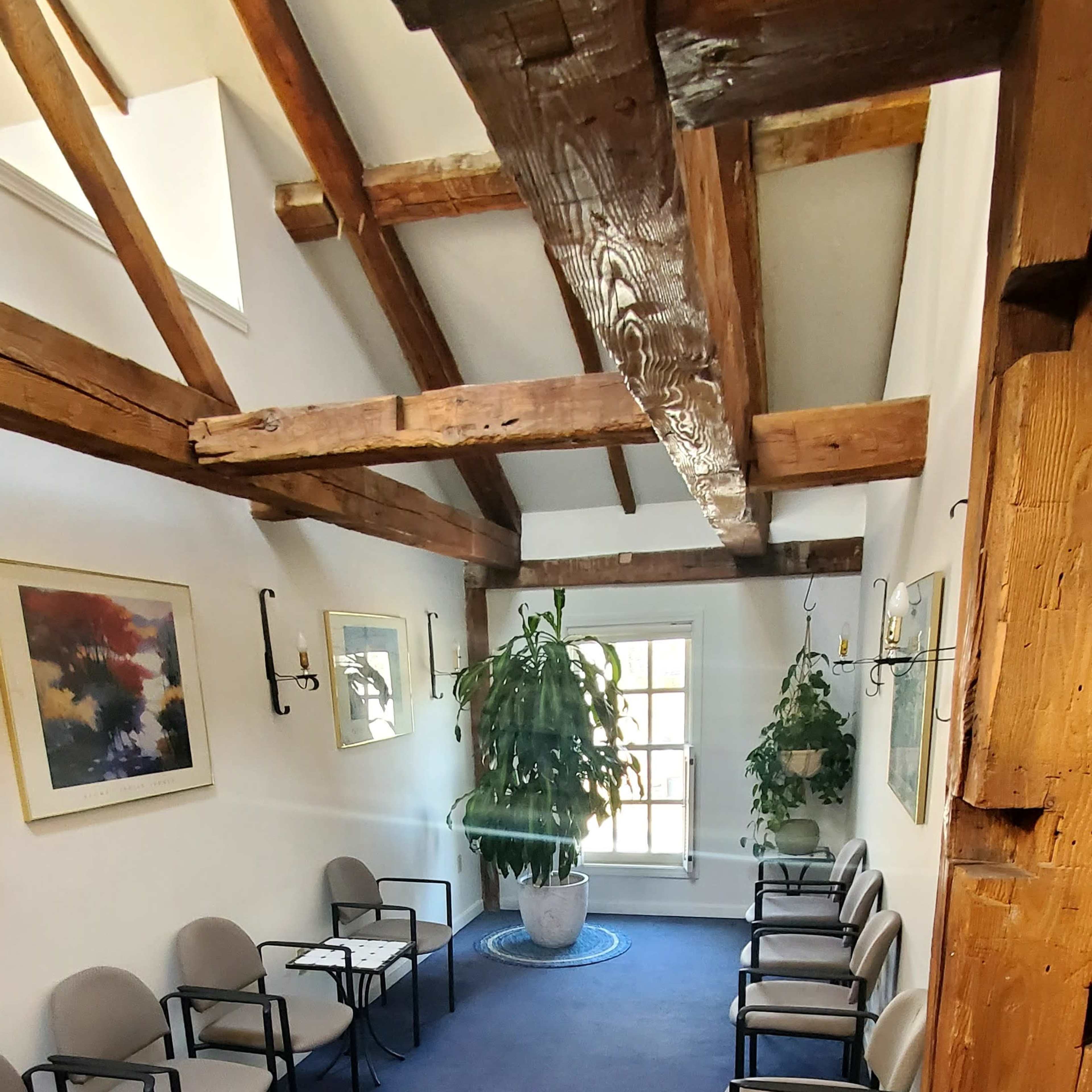 A spacious waiting area with wooden beams on the ceiling, potted plants, and several chairs arranged along the walls.