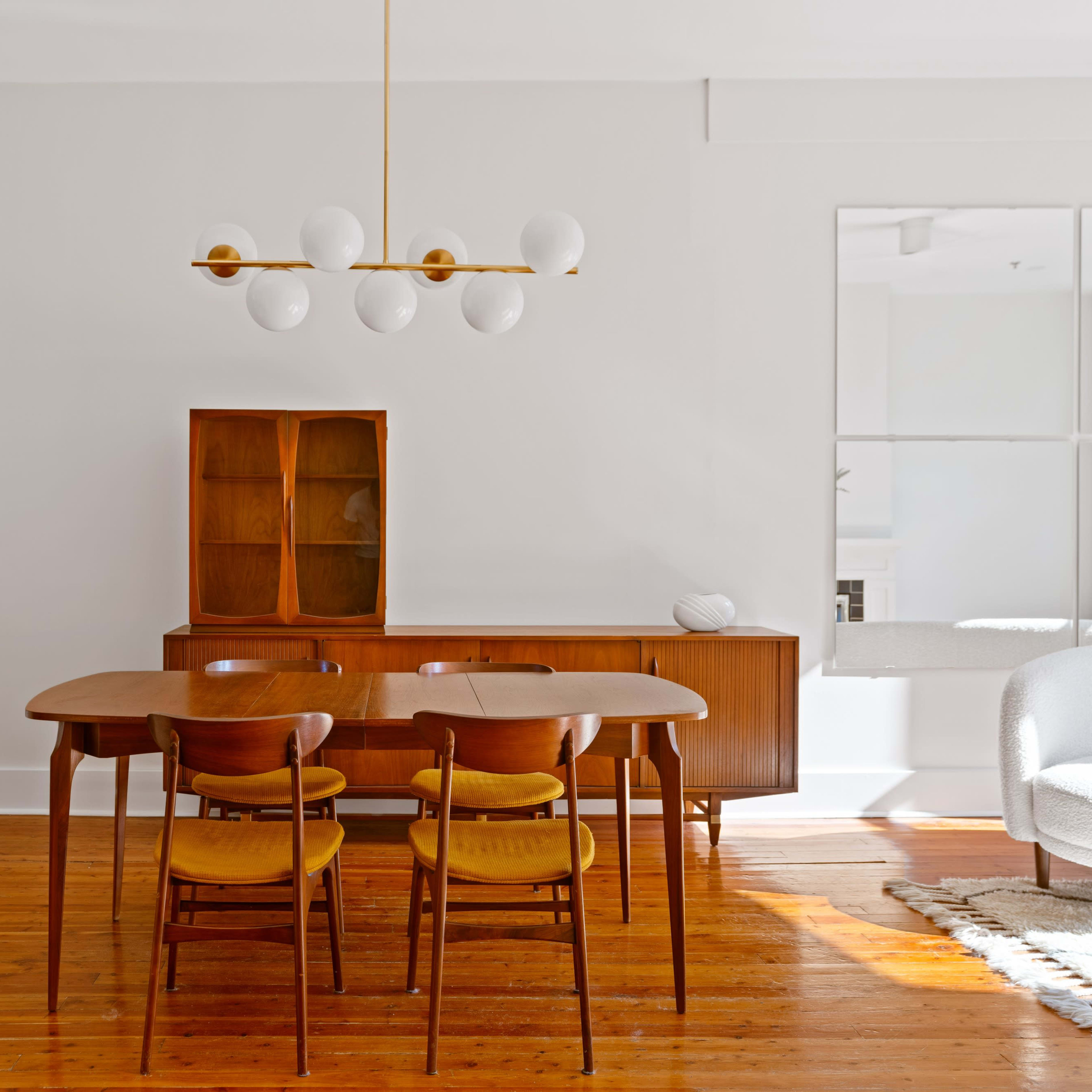A modern dining area featuring a wooden table with four chairs, a sideboard, and a ceiling light fixture with round white bulbs.