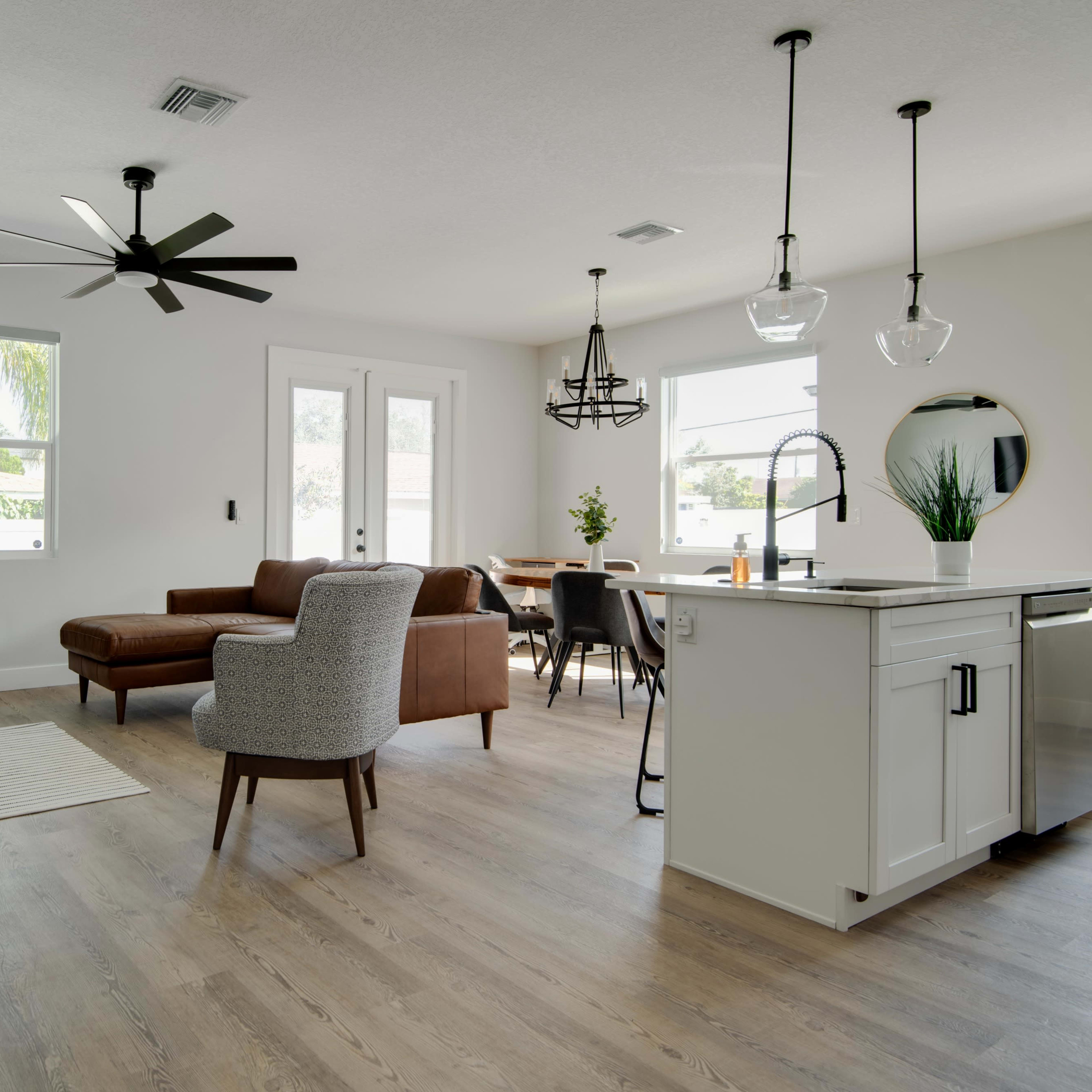 A modern living and dining area with a sectional sofa, dining table, ceiling fans, and large windows.
