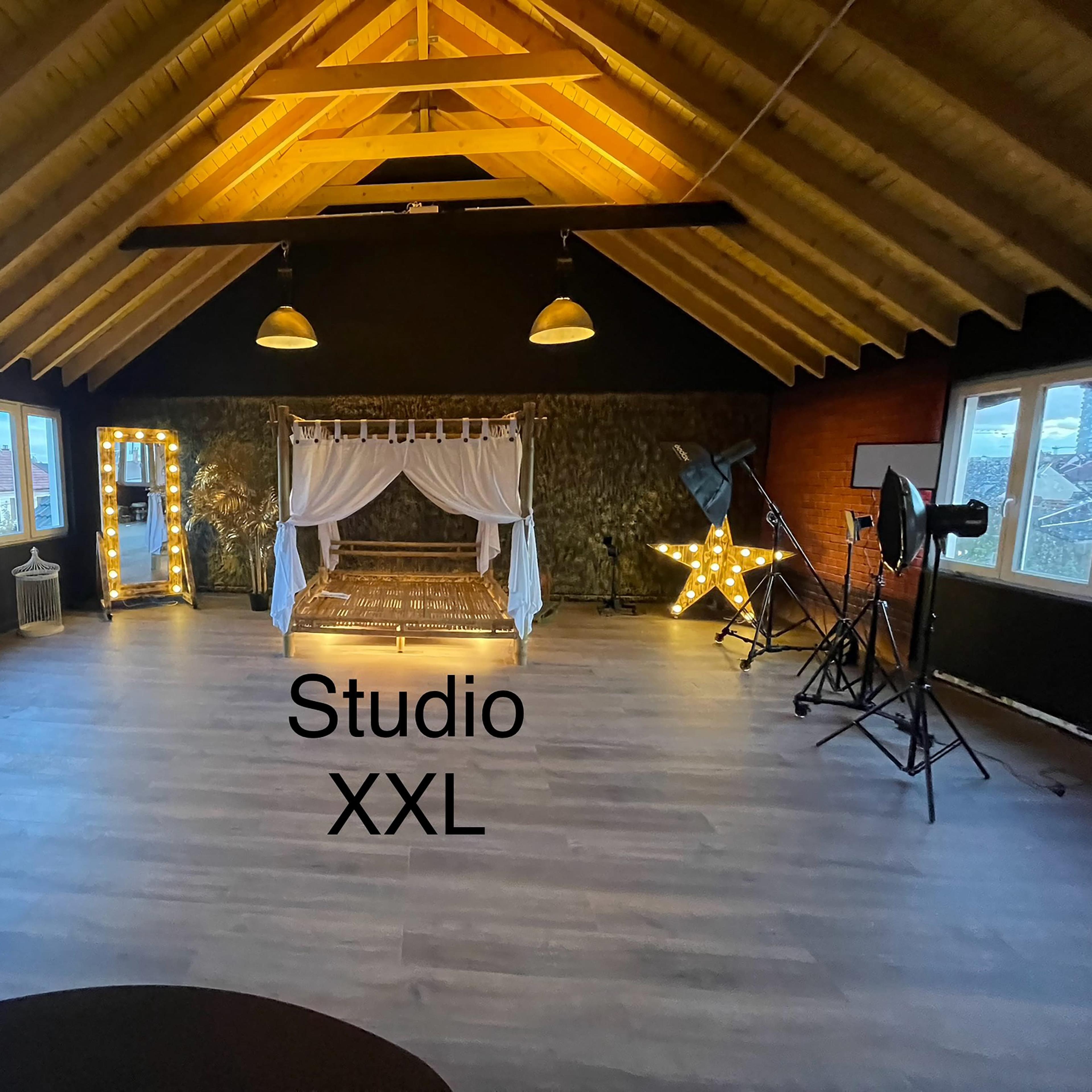 A spacious studio with wooden beams, featuring a decorated bed frame with curtains, illuminated letters, and photography equipment.