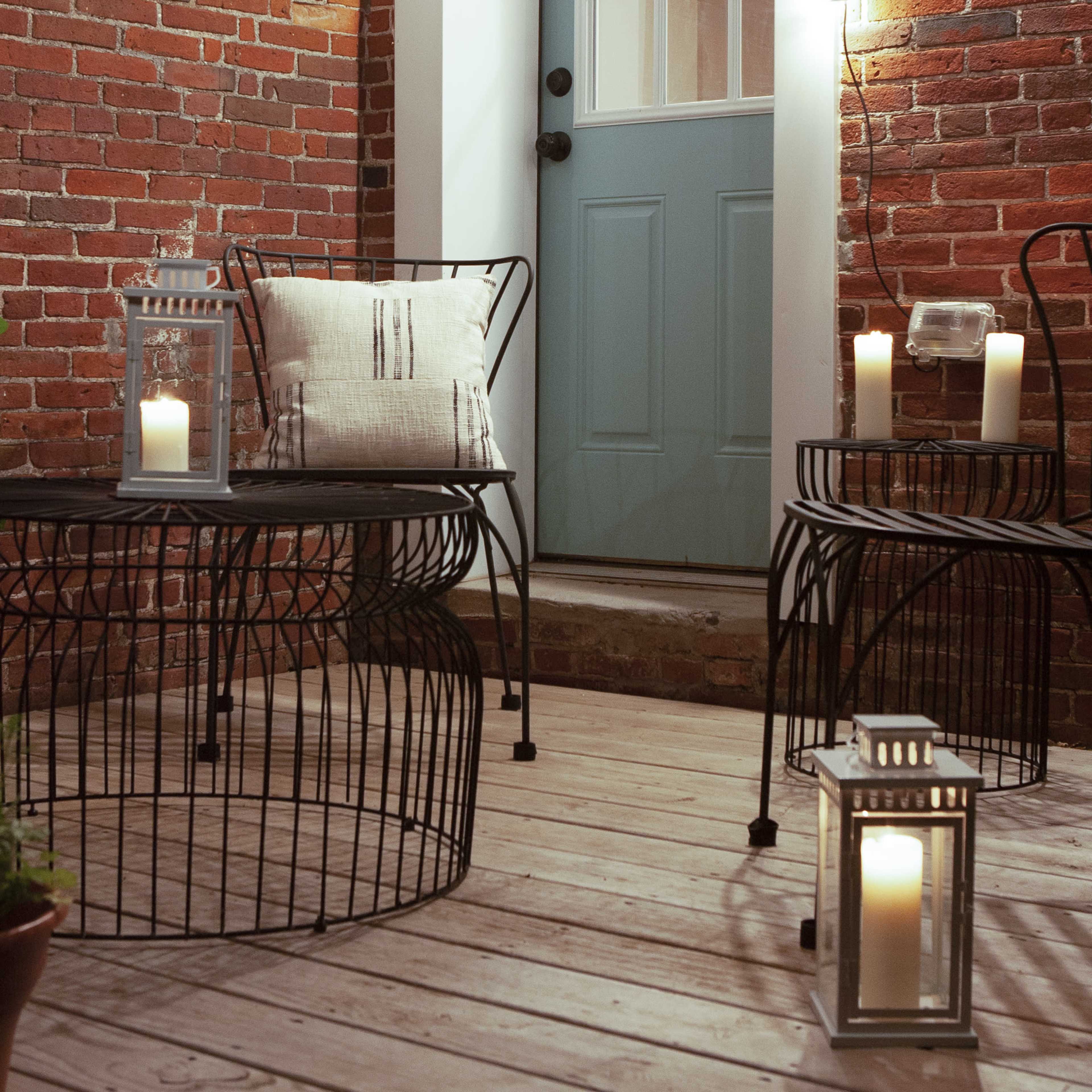 A cozy outdoor space featuring a blue door, brick walls, two wire tables, and decorative lanterns with candles.