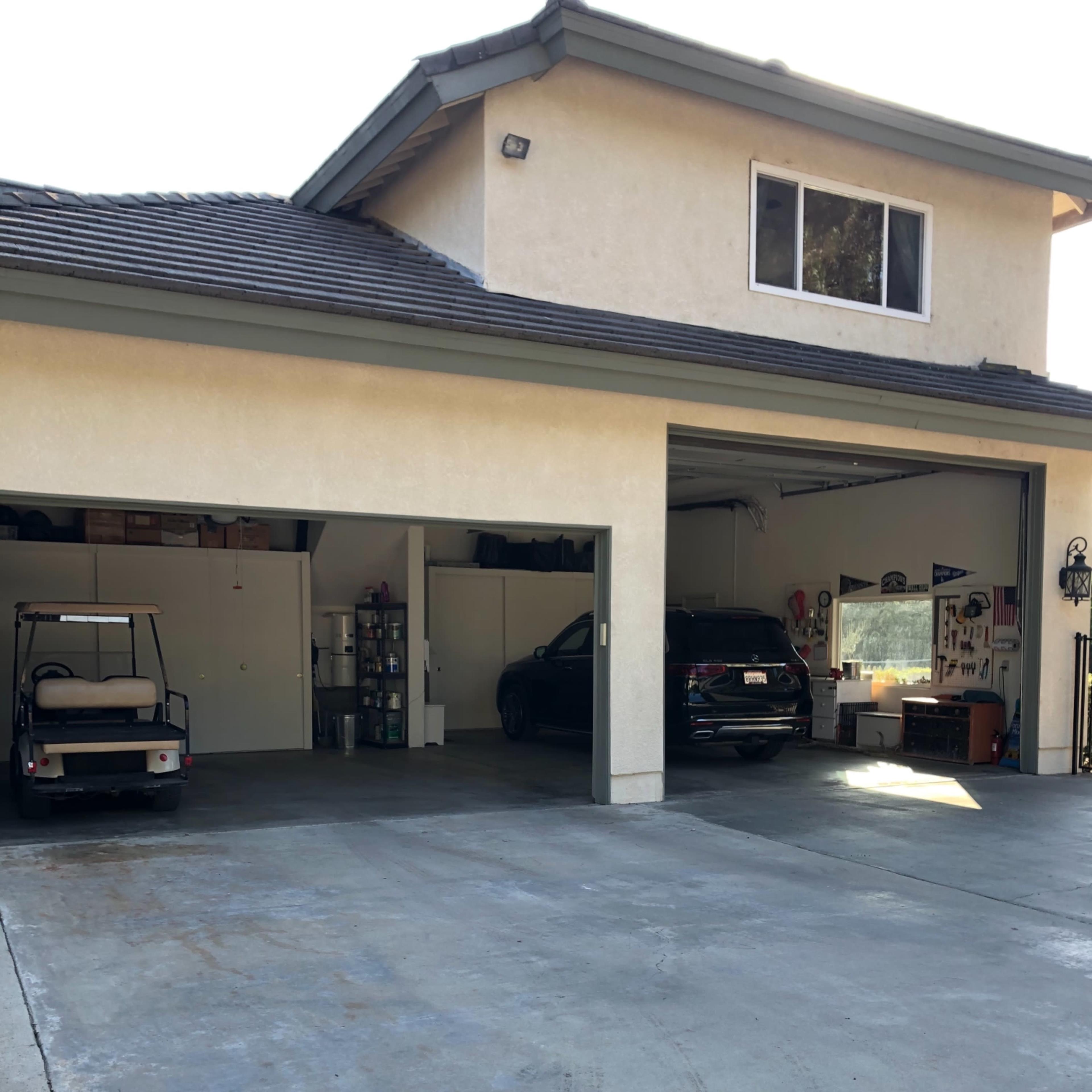 A two-car garage with one side open, containing a black vehicle and storage shelves, while a golf cart is parked outside.