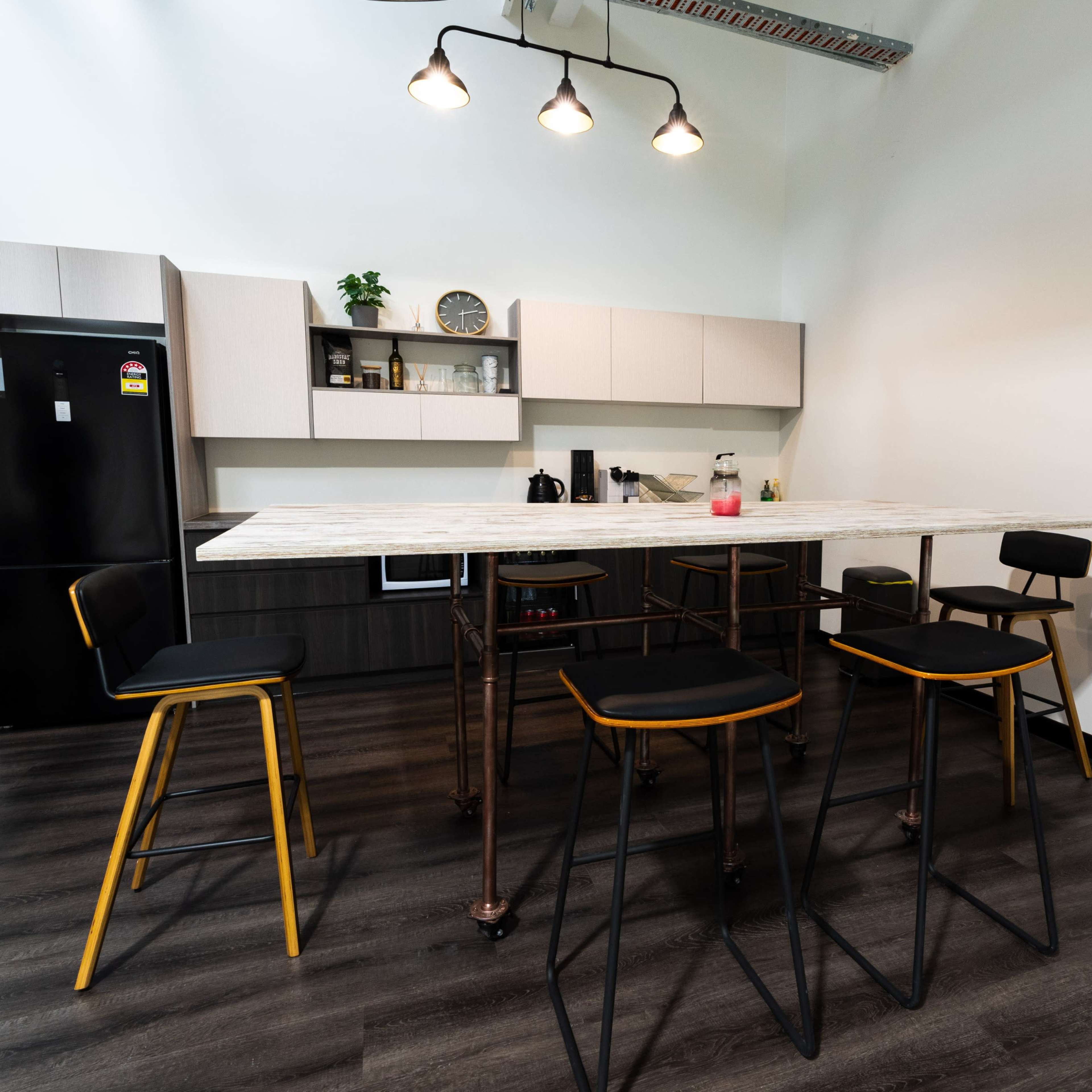 A modern kitchen features a high countertop with several stools, sleek cabinetry, and a refrigerator against the wall.