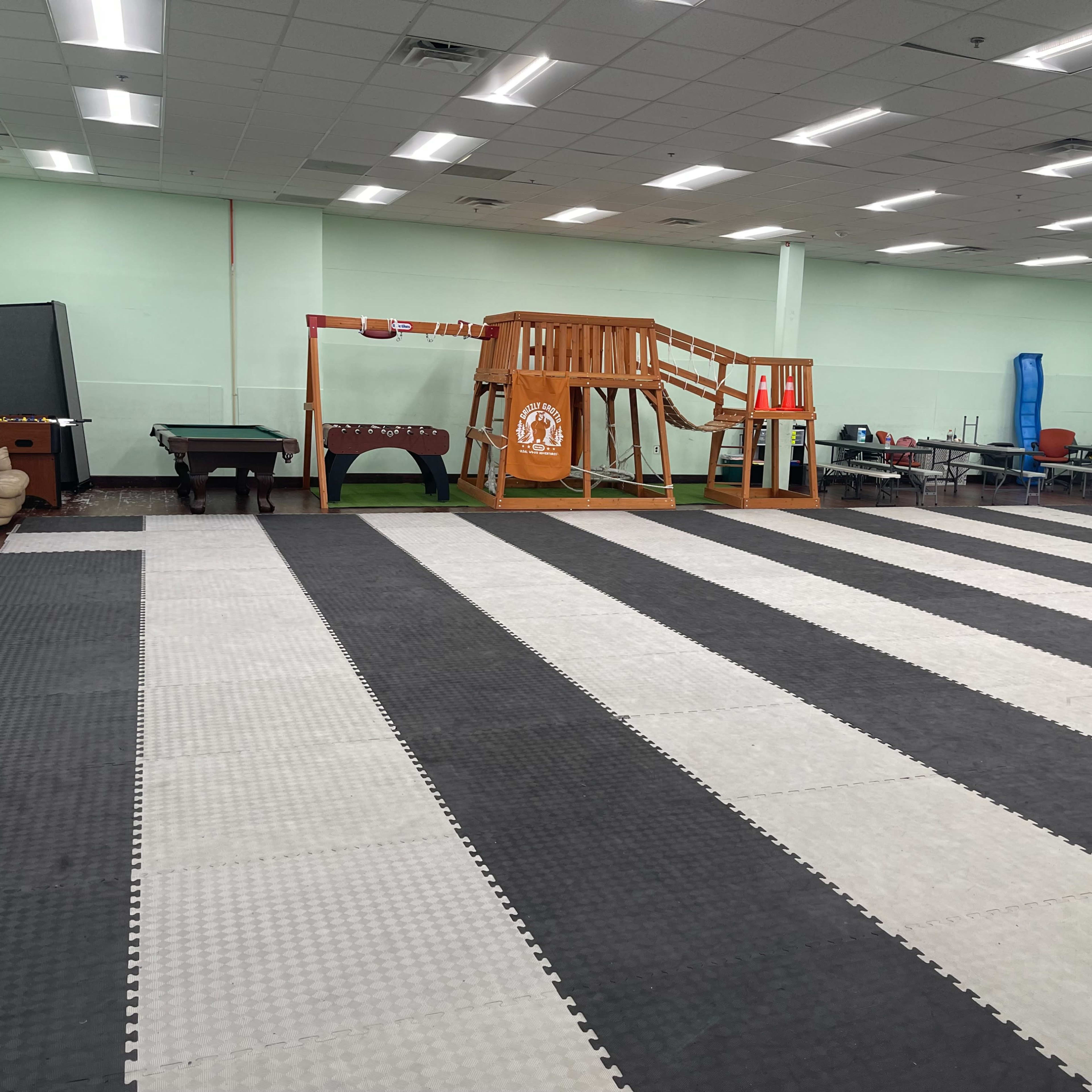 A large room with alternating black and white mats, featuring a playground structure and various furniture along the walls.
