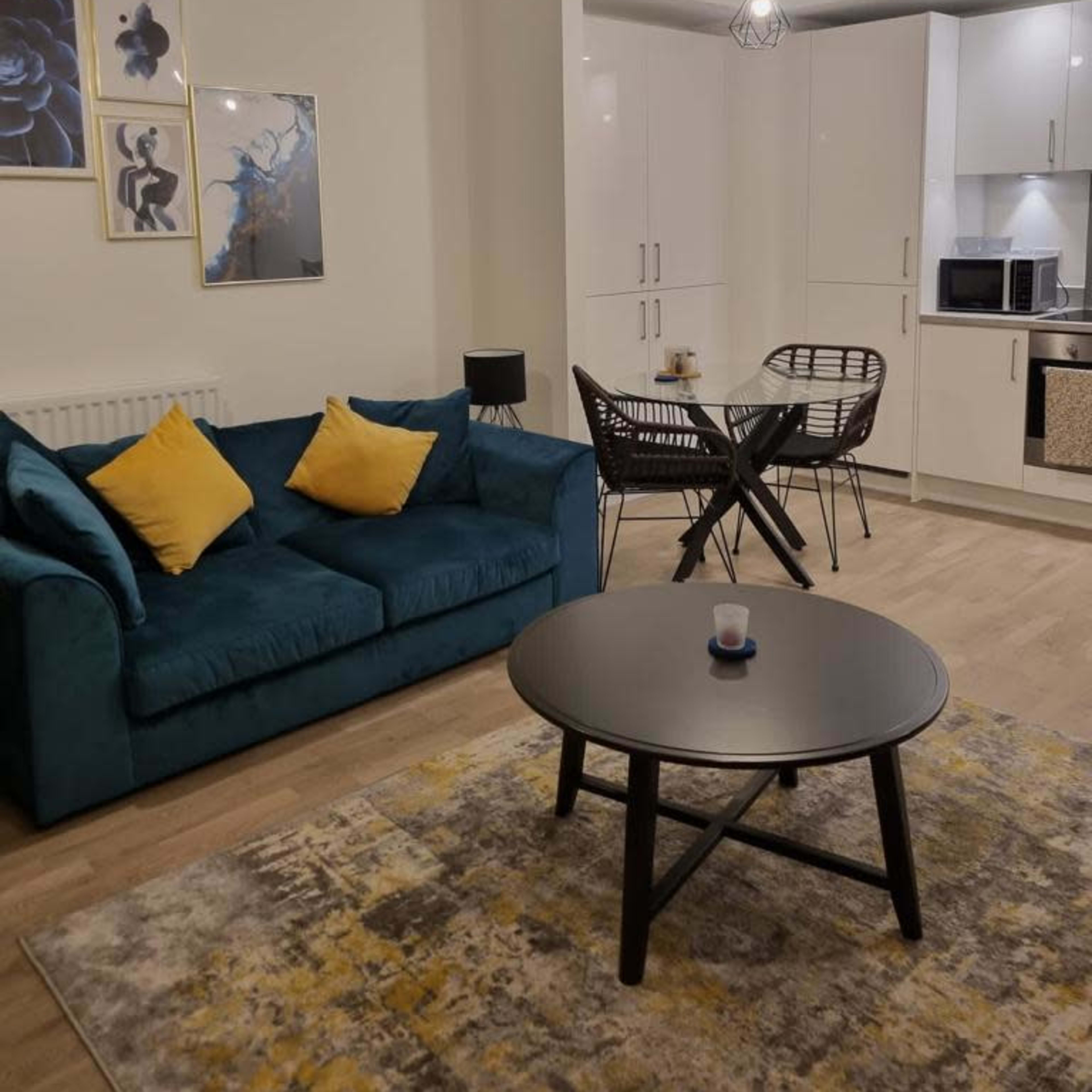 A modern living room with a teal sofa, a round black table, and a patterned rug, complemented by wall art and pendant lighting.
