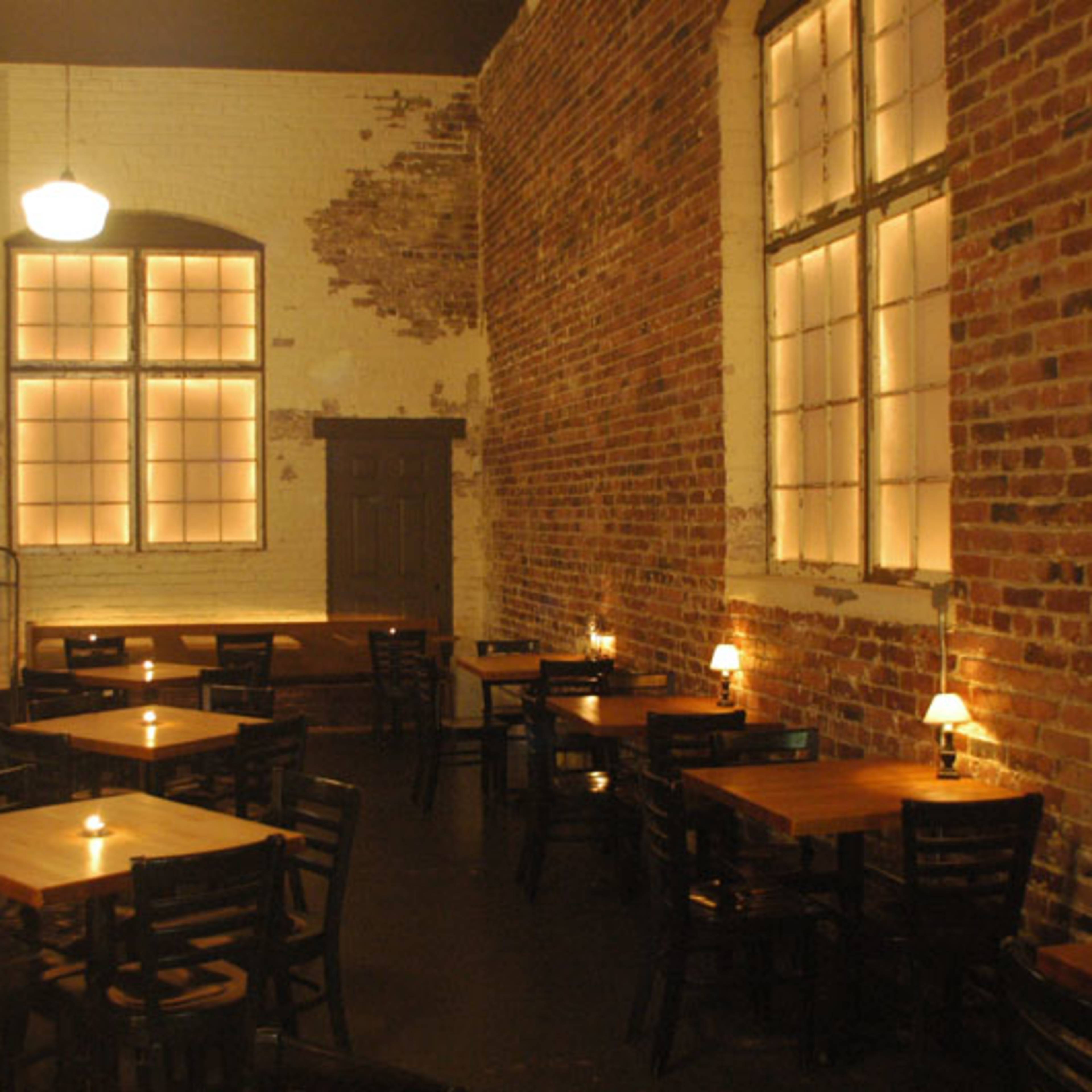 A rustic restaurant interior with brick walls, wooden tables, and soft lighting from candles.