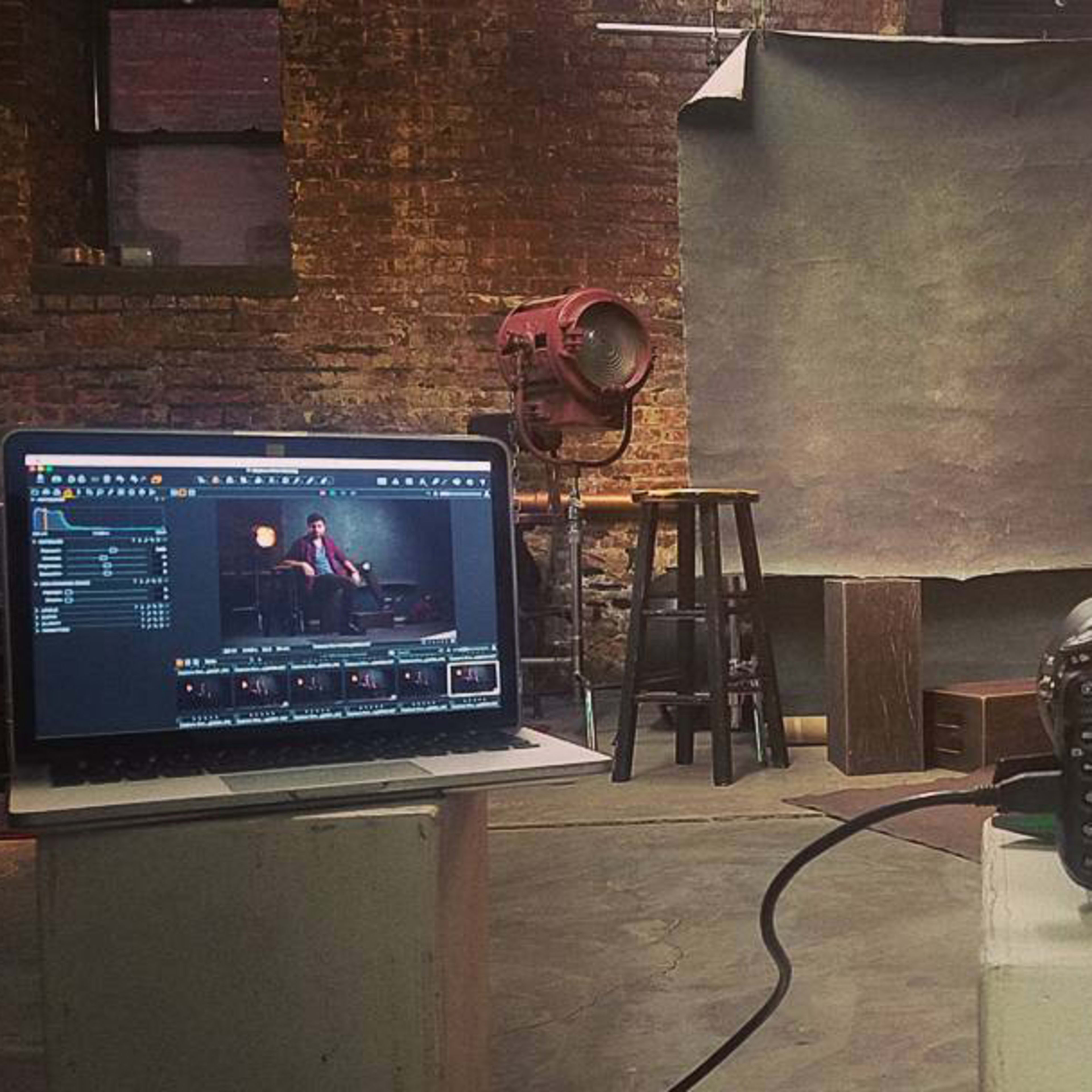 A camera is positioned on a pedestal facing a backdrop, while a laptop displays the camera's settings and images in a photography studio.