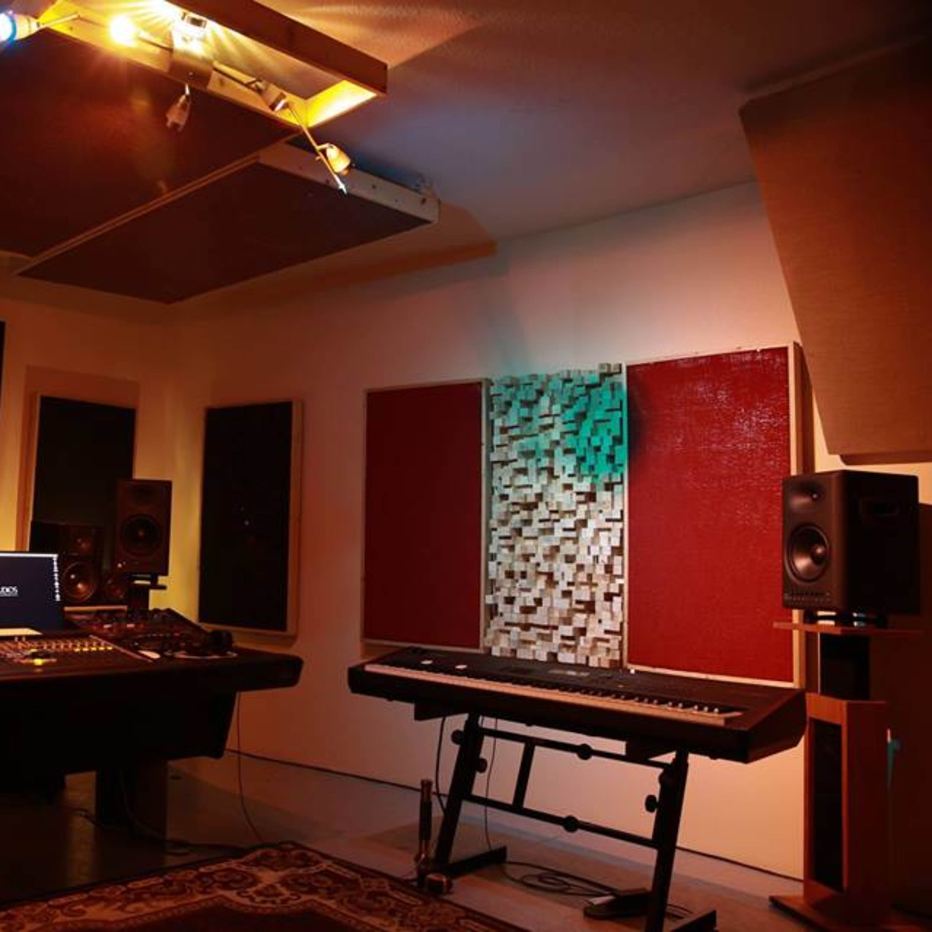 A recording studio featuring a mixing console, studio monitors, and a keyboard with soundproof panels on the walls.