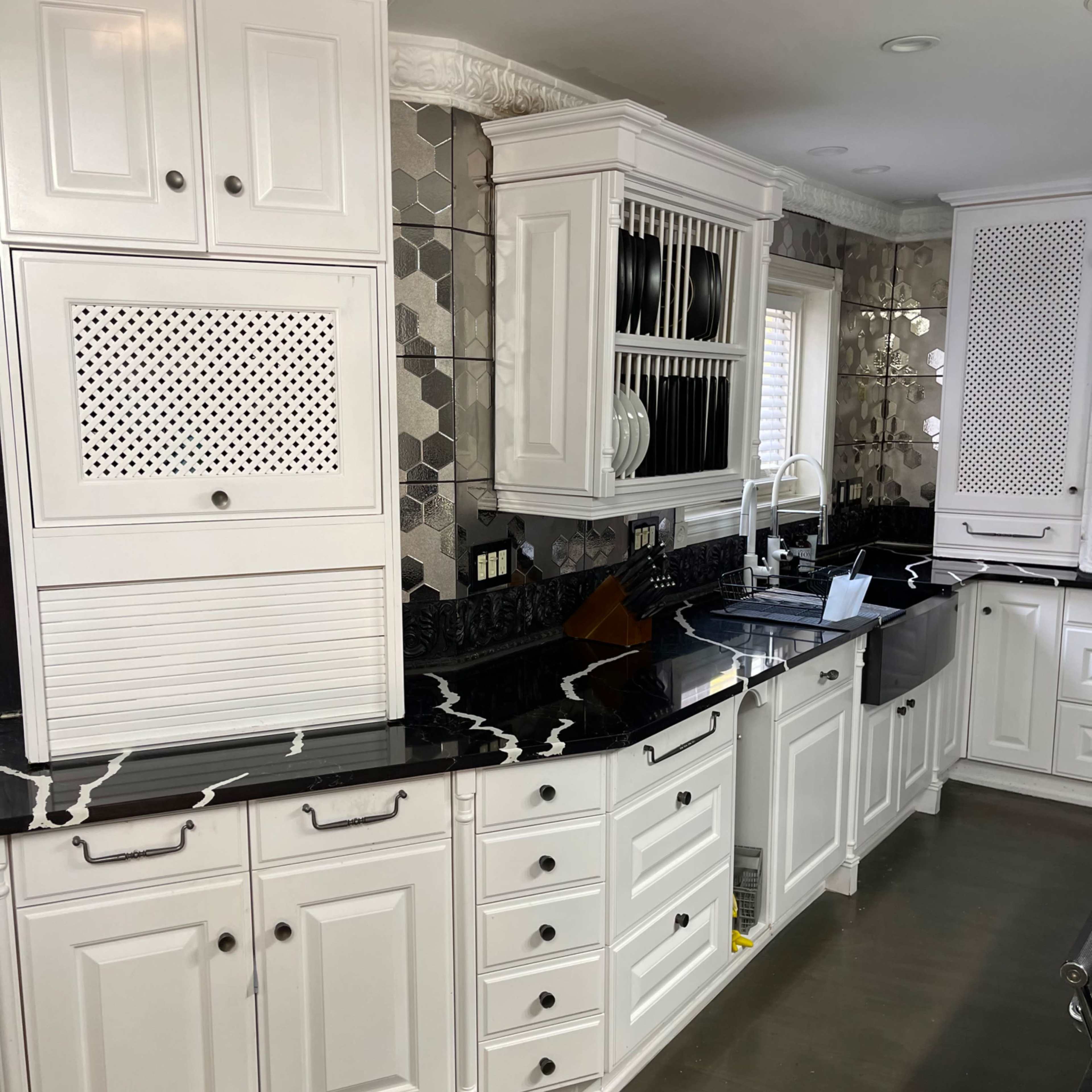 A modern kitchen featuring white cabinetry, black countertops, and a patterned backsplash.