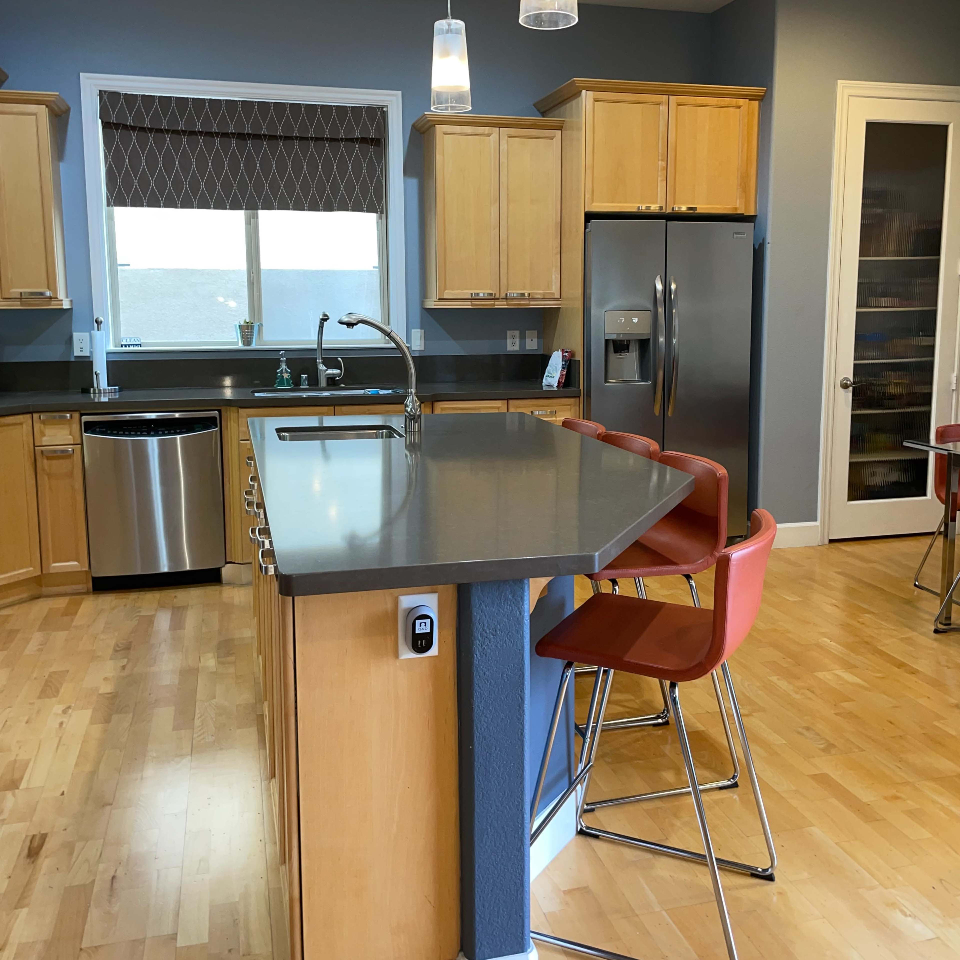A modern kitchen with wooden cabinets, stainless steel appliances, a gray countertop, and a central island with barstool seating.