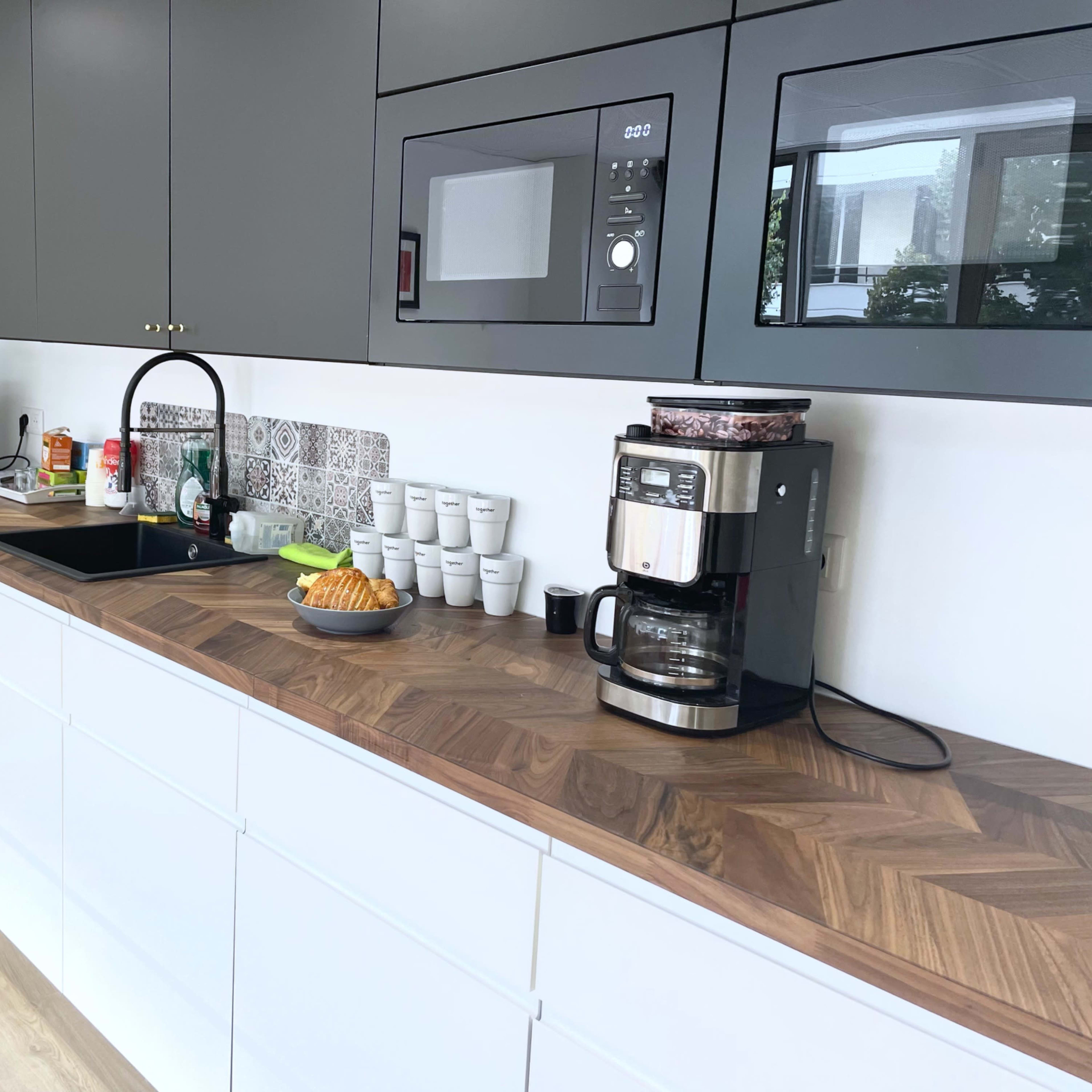 A modern kitchen with gray cabinets, a wooden countertop, a coffee maker, a microwave, and a sink, alongside various kitchen appliances and utensils.