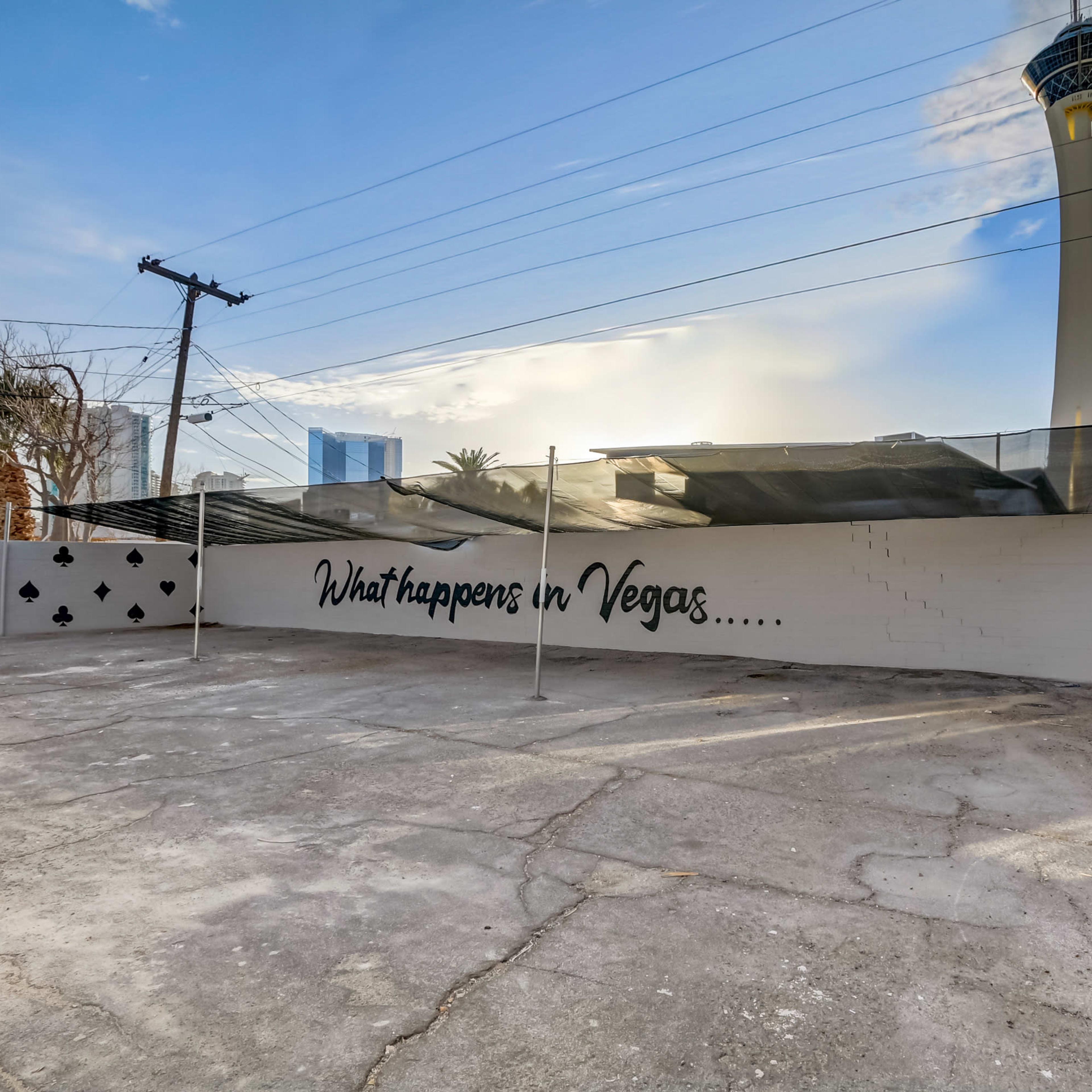 An empty concrete lot with a wall displaying the phrase "What happens in Vegas....." and the Stratosphere Tower in the background.